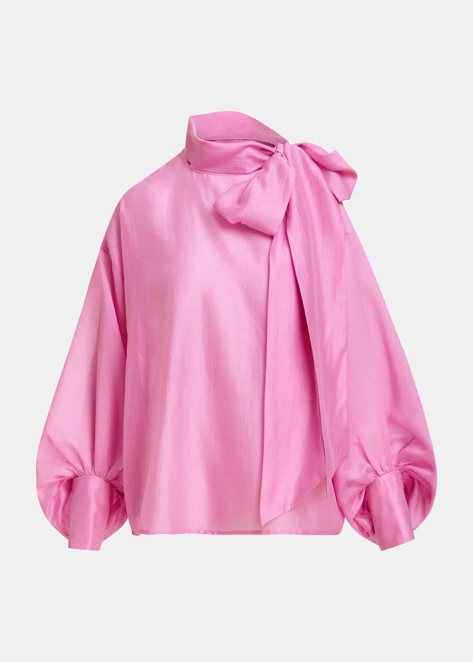 A bright pink satin blouse with a large bow at the collar and voluminous long sleeves with gathered cuffs, shown on a light gray background.