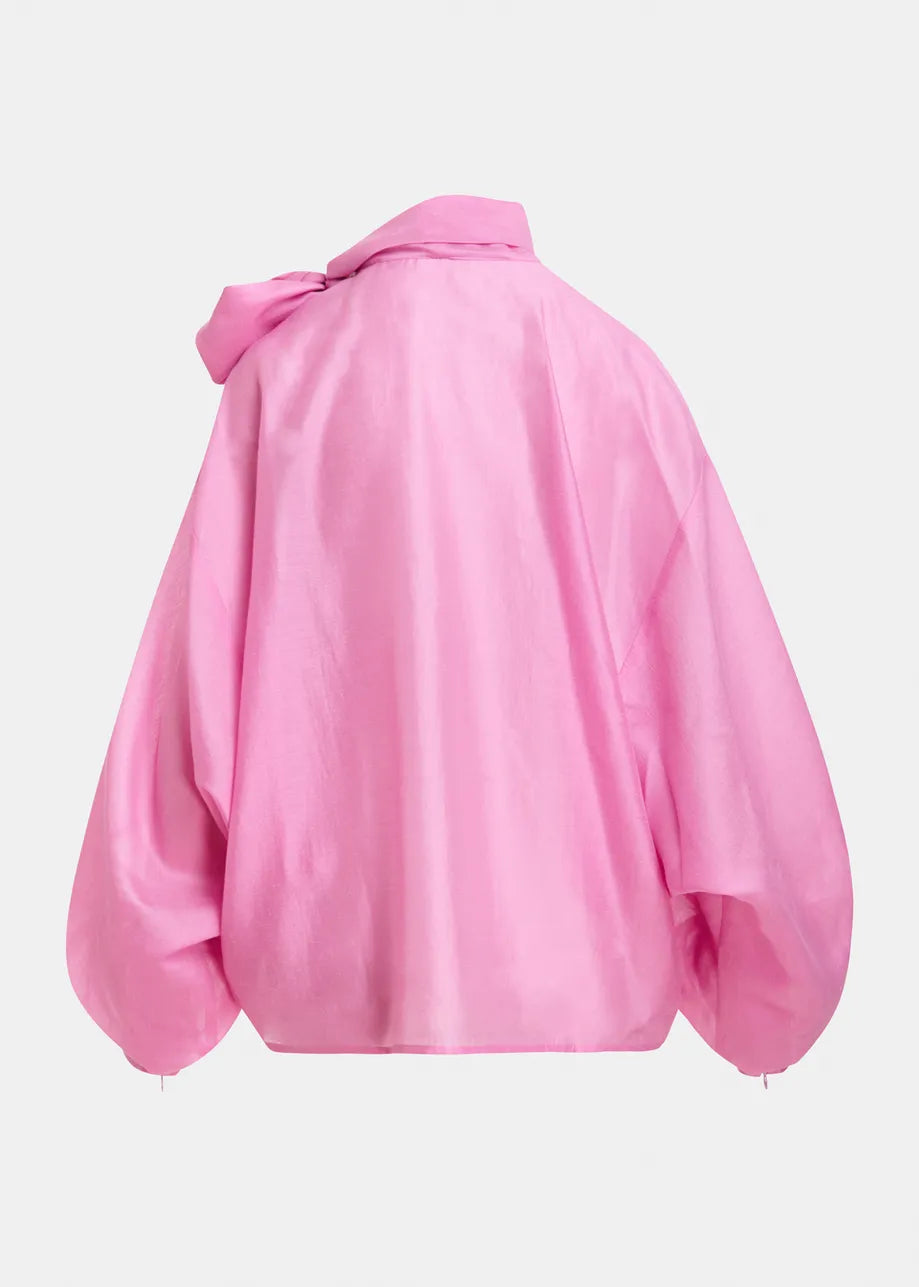 A bright pink oversized jacket with voluminous balloon sleeves and a large bow detail on the left shoulder, shown from the back against a light gray background.