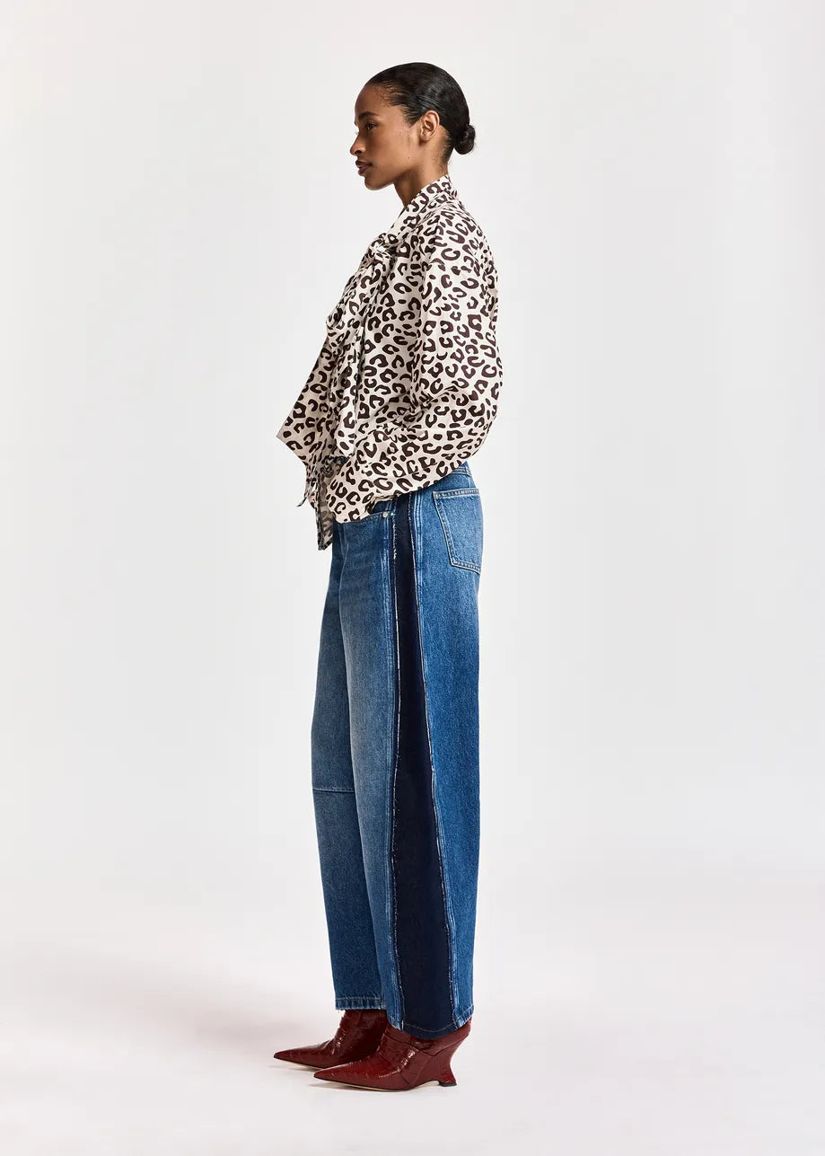 A model shown in profile wearing a leopard-print long-sleeve shirt, barrel-leg blue jeans, and burgundy pointed-toe heeled boots against a plain white studio background.