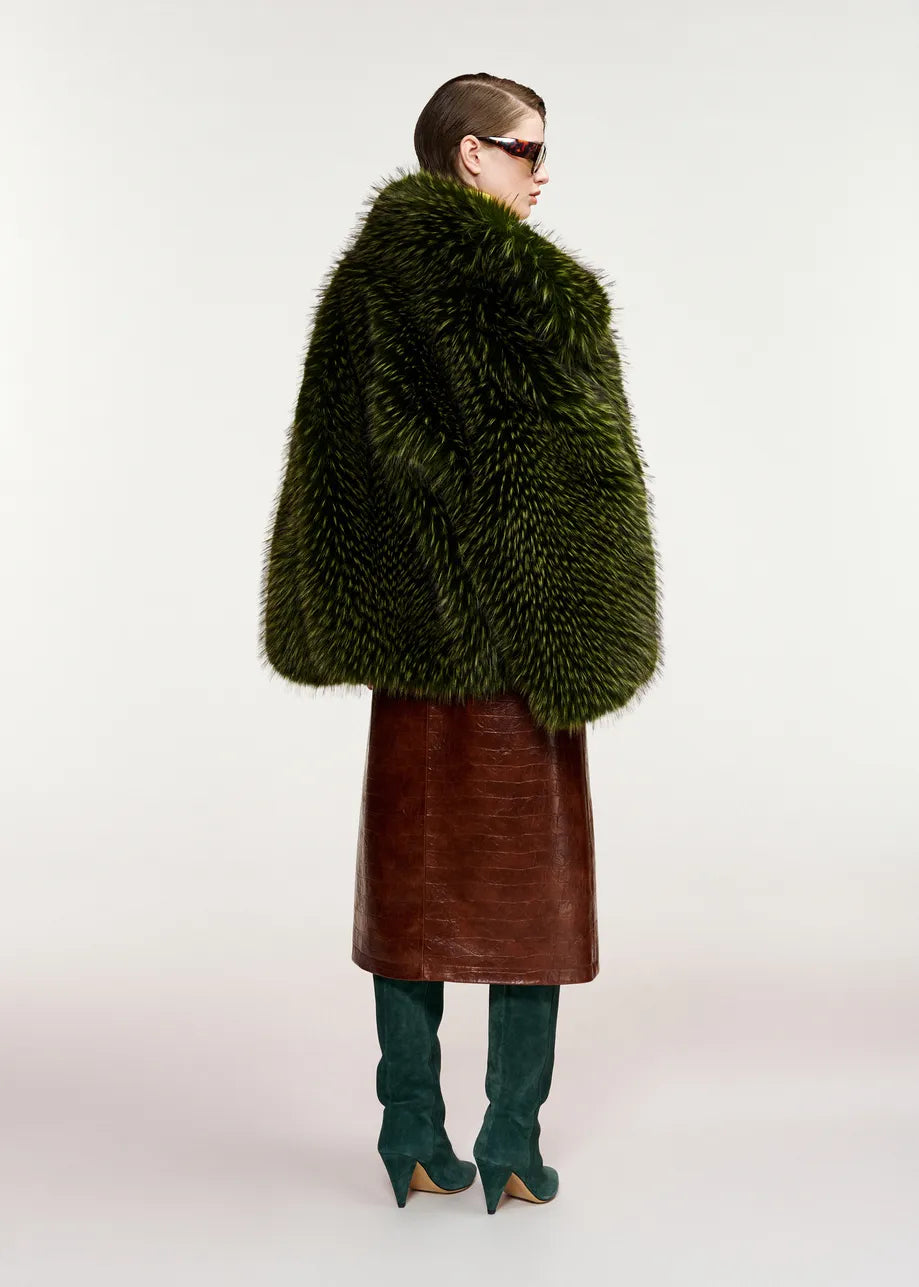 A person wearing an oversized silhouette featuring the Essentiel Antwerp Kastanje Oversized Faux Fur Jacket in green, styled with a brown leather skirt, teal high-heeled boots, and sunglasses, stands against a light background.