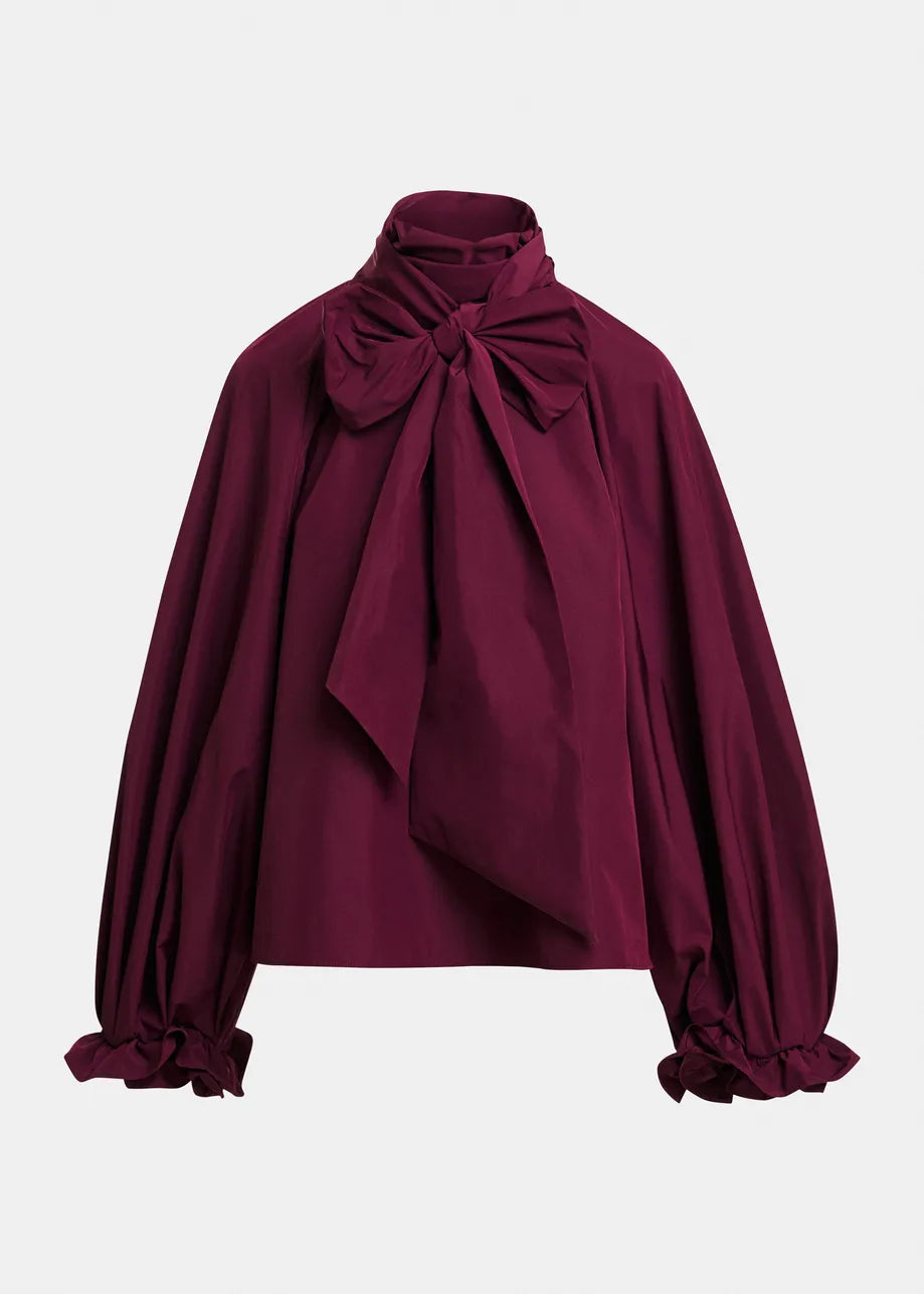 Introducing the Keily Pussy Bow Tie Top by Essentiel Antwerp—a long-sleeve, oversized blouse in deep burgundy with a high neck and dramatic pussy-bow collar. Featuring gathered cuffs tied with matching bows, this elegant top is crafted from recycled polyester, offering a modern and sustainable take on classic style.