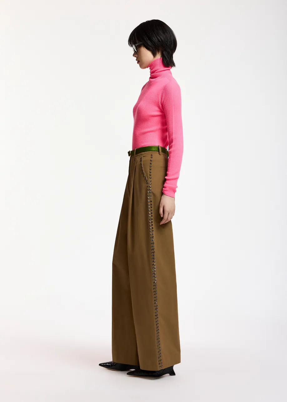 A person wearing the Essentiel Antwerp Kelmuse Knitted Pullover in pink and wide-leg brown pants stands in profile against a plain white background.