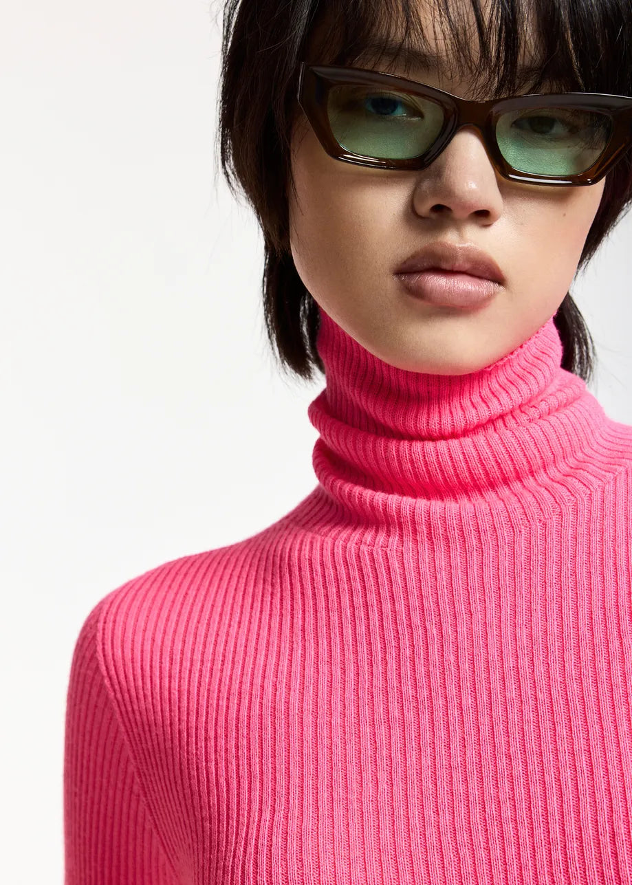 A person wearing the Essentiel Antwerp Kelmuse Knitted Pullover in pink and rectangular dark sunglasses stands against a plain background.
