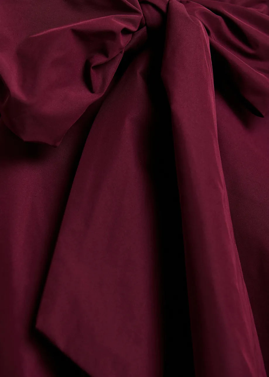 A close-up of draped deep burgundy fabric with soft folds and a gathered knot at the top, filling the frame.