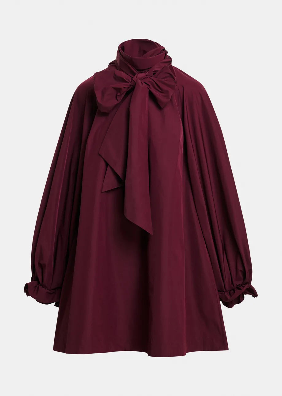 A deep burgundy long-sleeve blouse with a high gathered neck, large bow detail at the collar, and ruffled cuffs, shown against a plain light gray background.