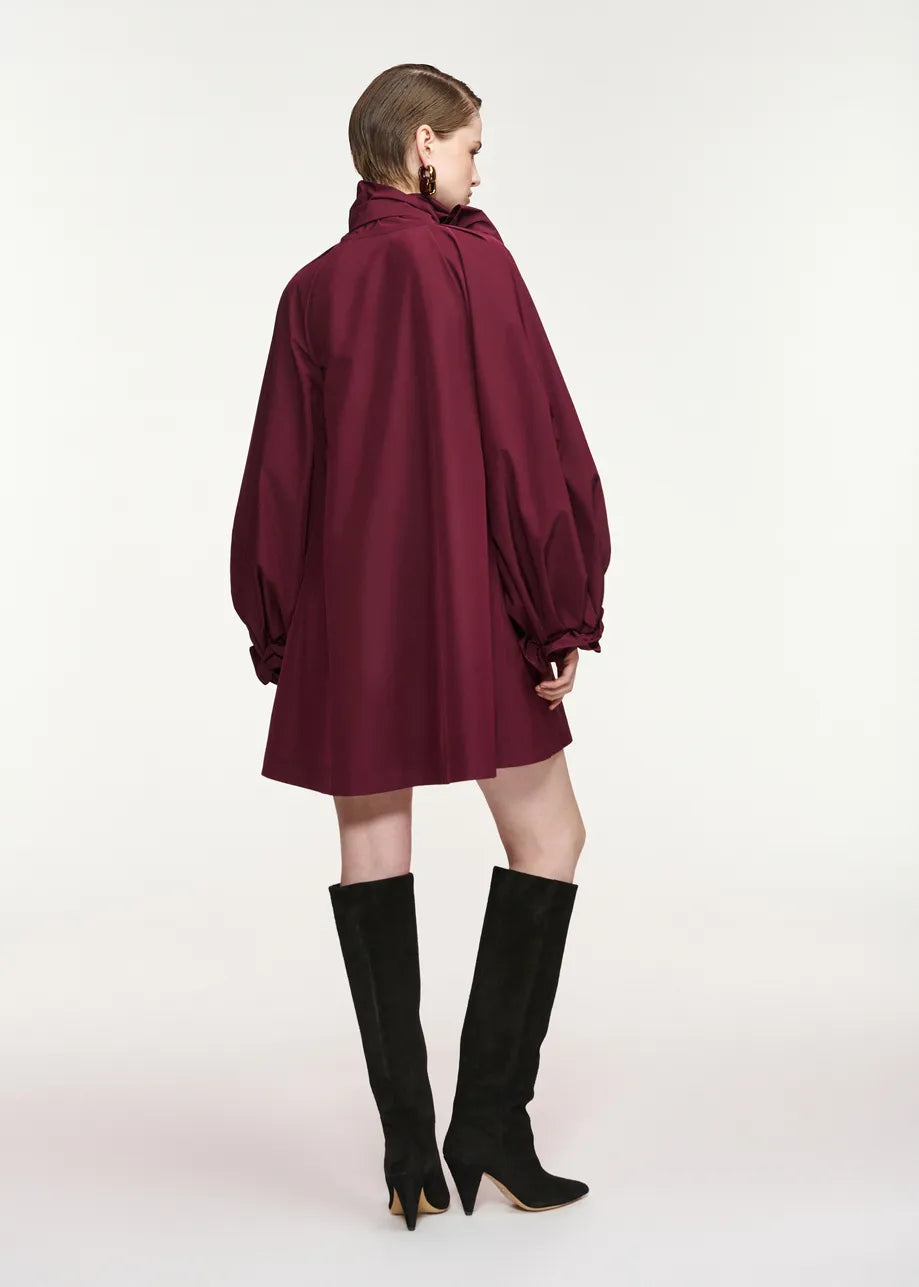 A model shown from the back wearing a burgundy oversized long-sleeve mini dress with balloon sleeves and black knee-high boots, set against a plain white studio background.