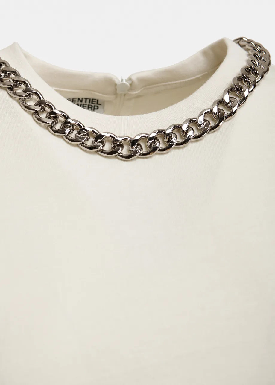 Close-up of a cream-colored t-shirt with a prominent chunky silver chain necklace styled around the collar, on a light gray background.