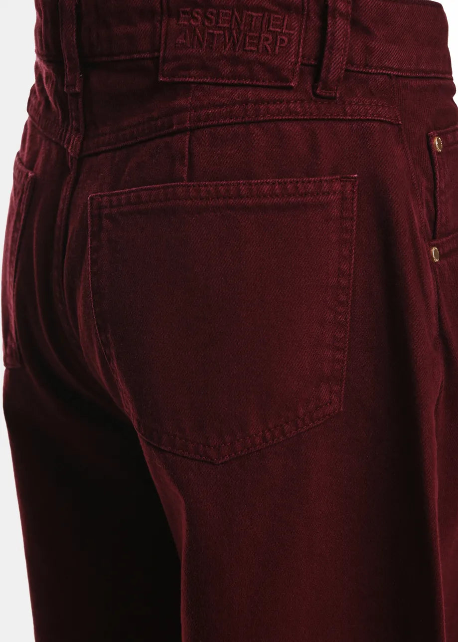 Close-up of the back of a person wearing Essentiel Antwerp Kokos Colour Denim Barrel Leg Jeans in burgundy, featuring a visible back pocket and a branded patch above the pocket.