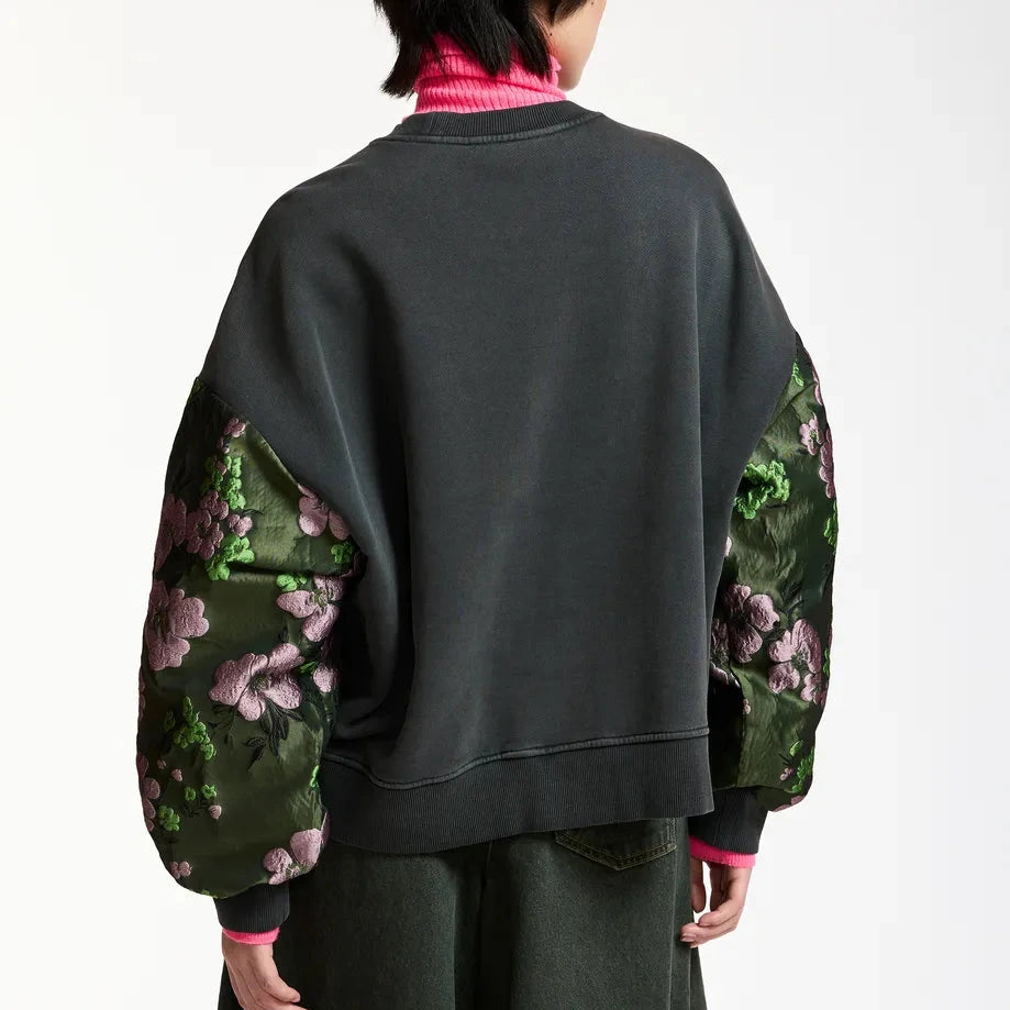 A person seen from the back wears the Essentiel Antwerp Kueer Sweater with jacquard floral-patterned green sleeves and a bright pink turtleneck layered underneath.