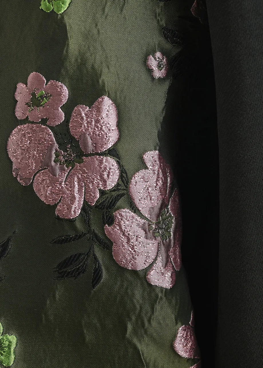 Close-up of the Kueer Sweater with Jacquard Sleeves by Essentiel Antwerp, featuring green floral jacquard fabric with pink embroidered flowers and black leaves, partially bordered by a solid black material on the right side.