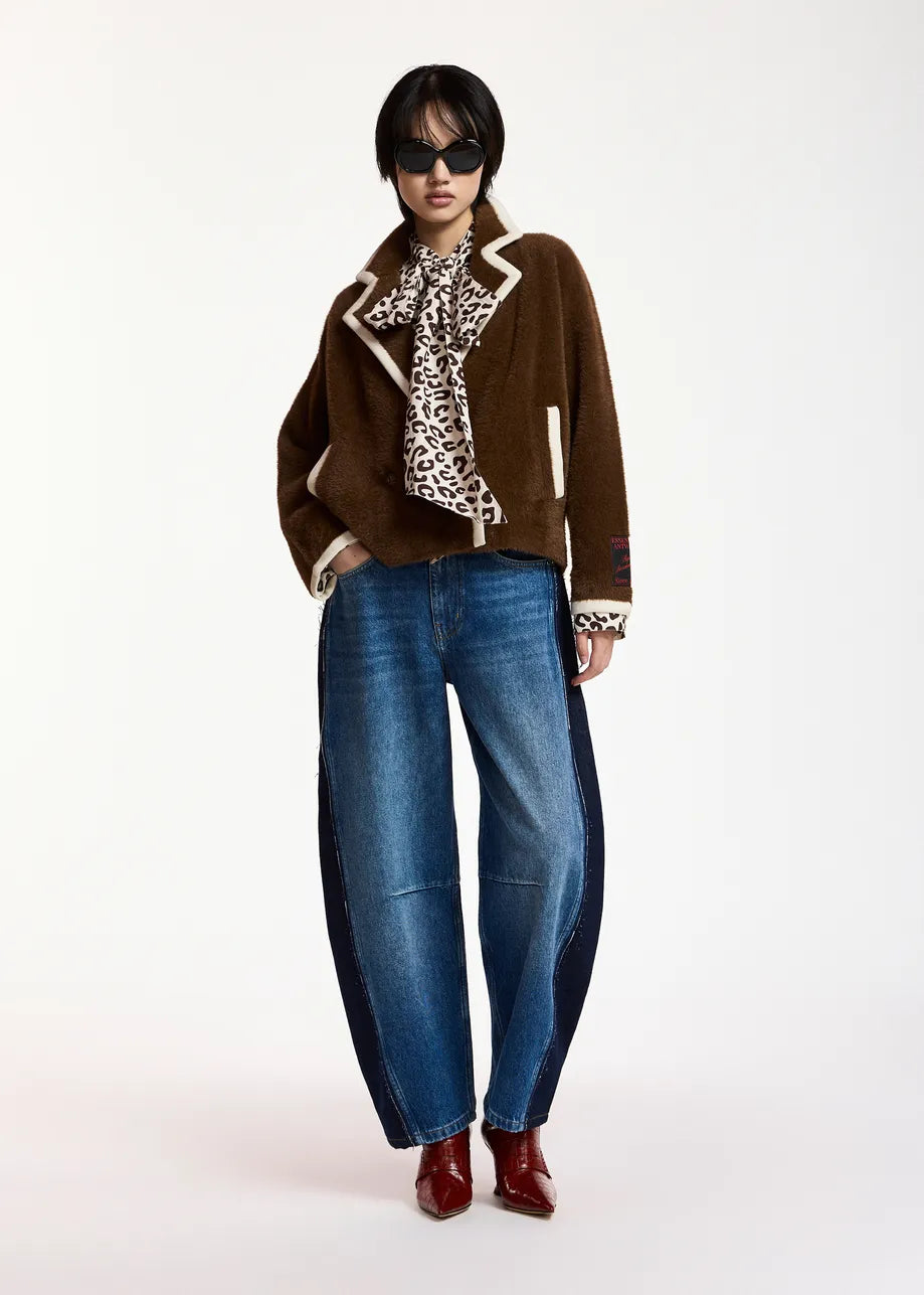 A model wearing a brown suede jacket with cream trim, blue wide-leg jeans, a leopard-print scarf, and red boots, photographed against a plain white studio background.