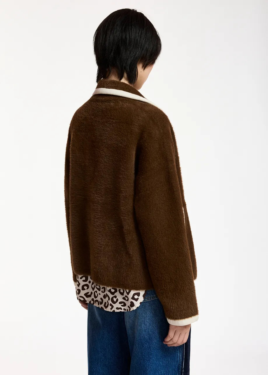A person shown from the back wearing a brown fuzzy cardigan over a cream and black patterned shirt, paired with blue jeans, against a plain white background.