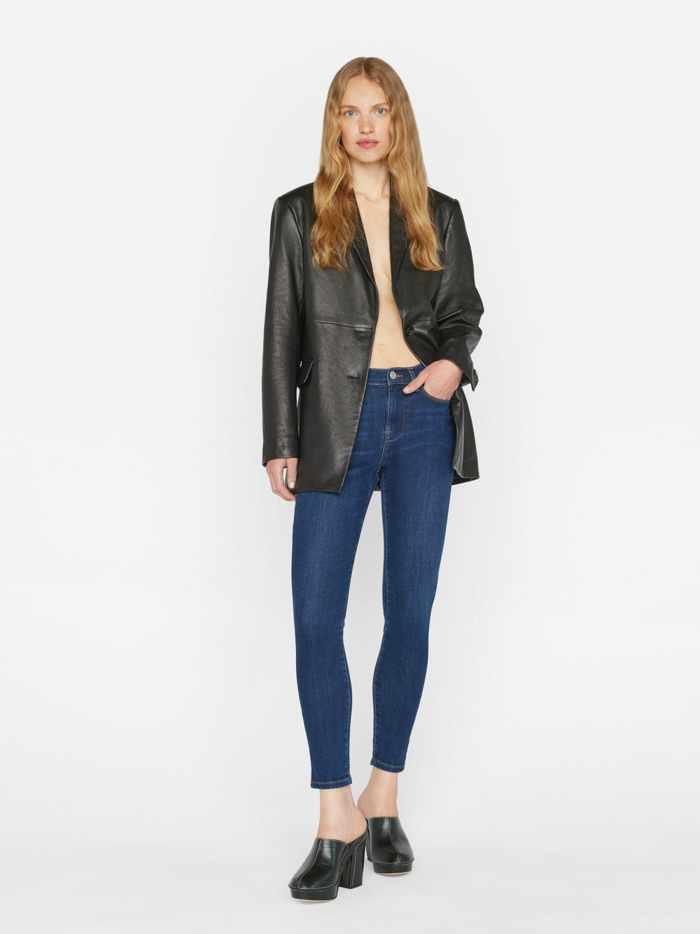 The model is wearing the Frame Le High Skinny Outseam Slit - Majesty jeans, a form-fitting silhouette made of sustainable stretch cotton blend and paired with a leather jacket.