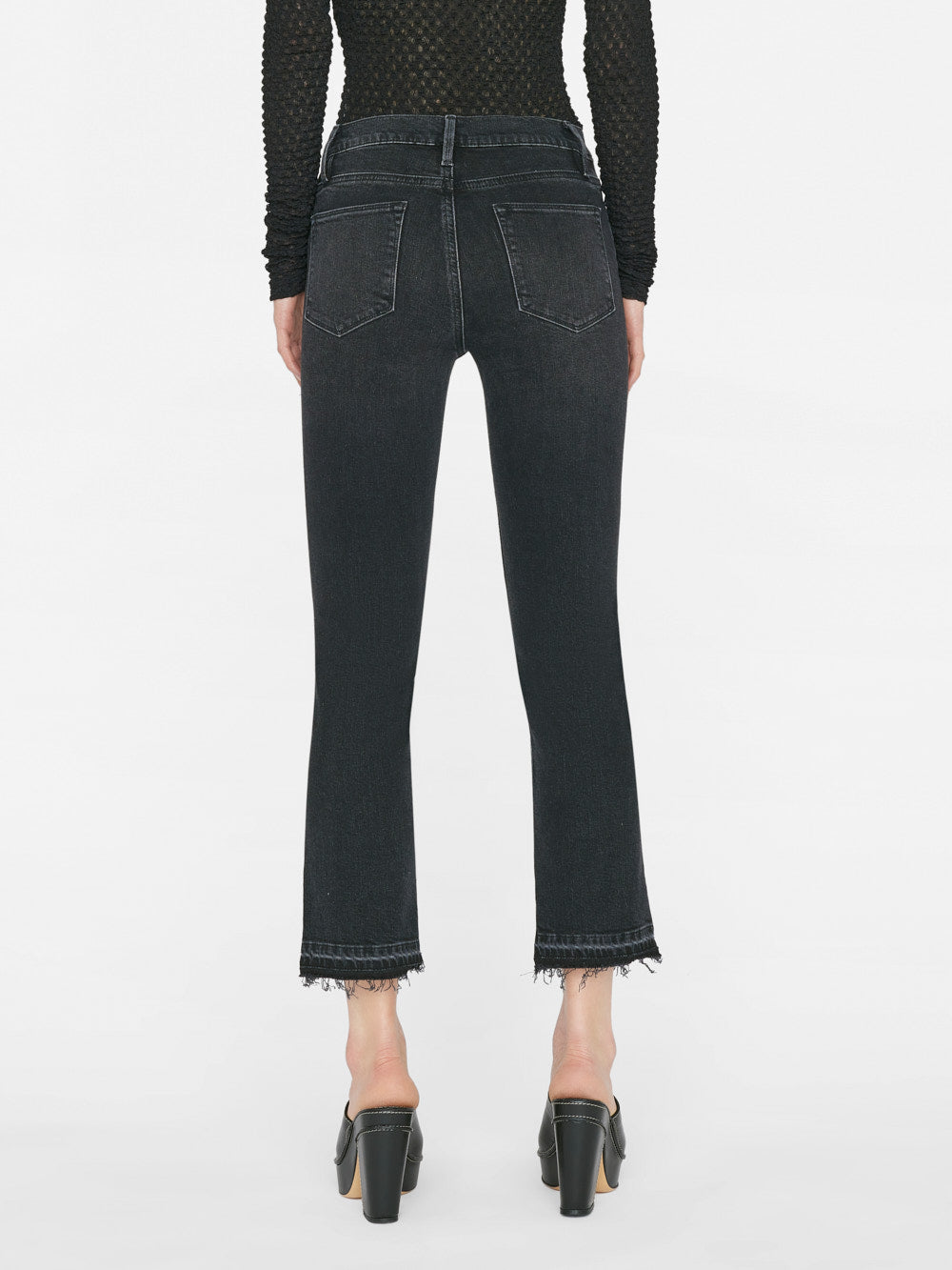 The back view of a woman wearing Frame Le High Straight Released Hem - Hutchison jeans with frayed hems.