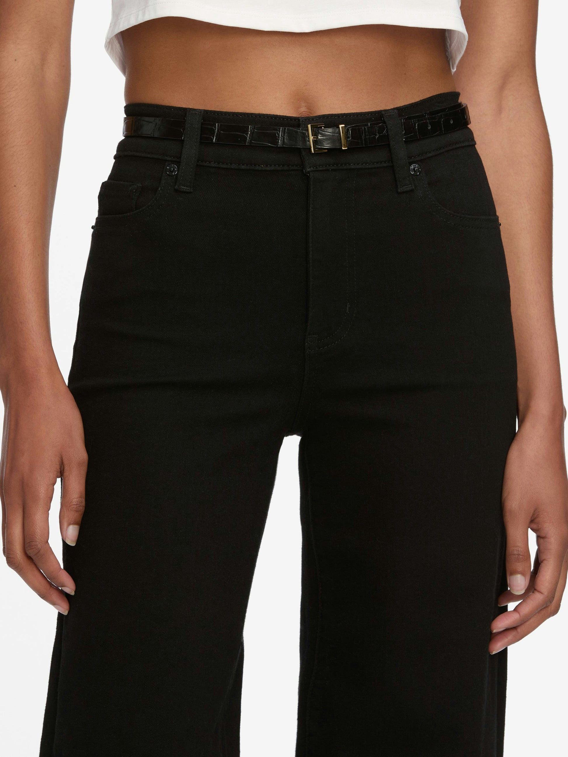 A person shown from the waist down wears Frame Le Slim Palazzo Jeans in black by Frame, styled with a black belt and a white cropped top.