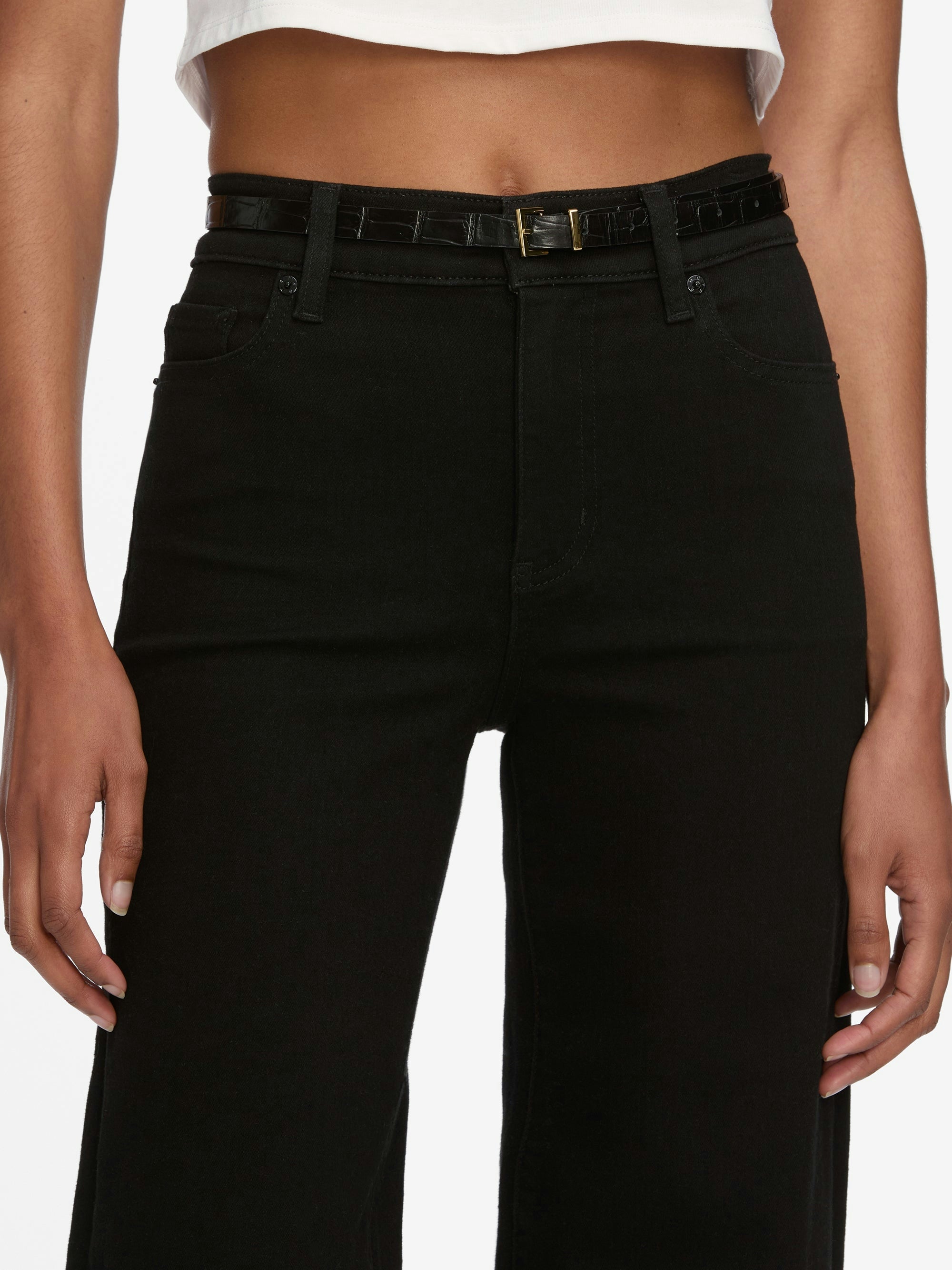 A person shown from the waist down wears Frame Le Slim Palazzo Jeans in black by Frame, styled with a black belt and a white cropped top.