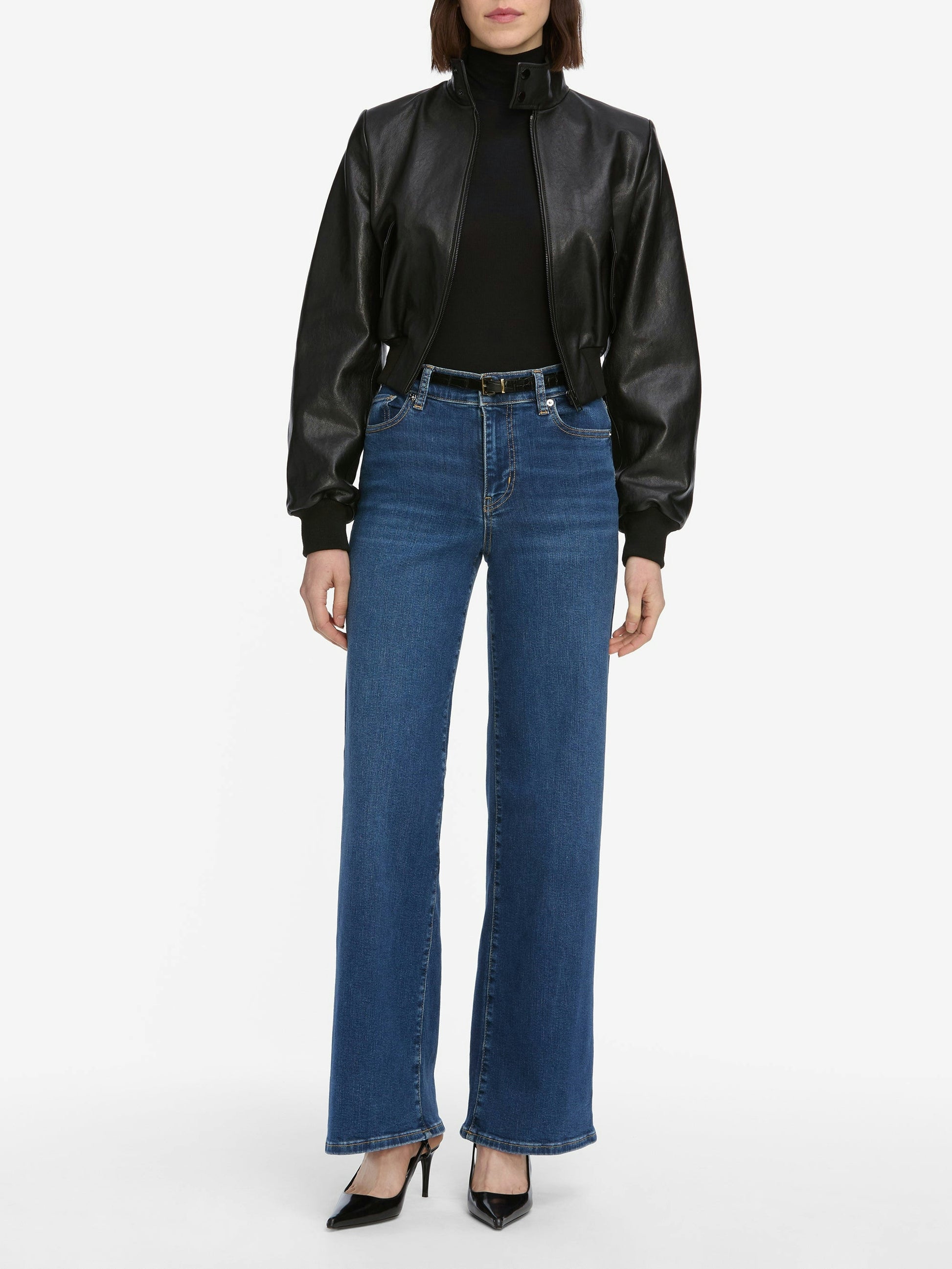 Person wearing a black leather jacket, black top, Frame Le Slim Palazzo Jeans - Femma by Frame, and black pointed-toe heels, standing against a plain white background.