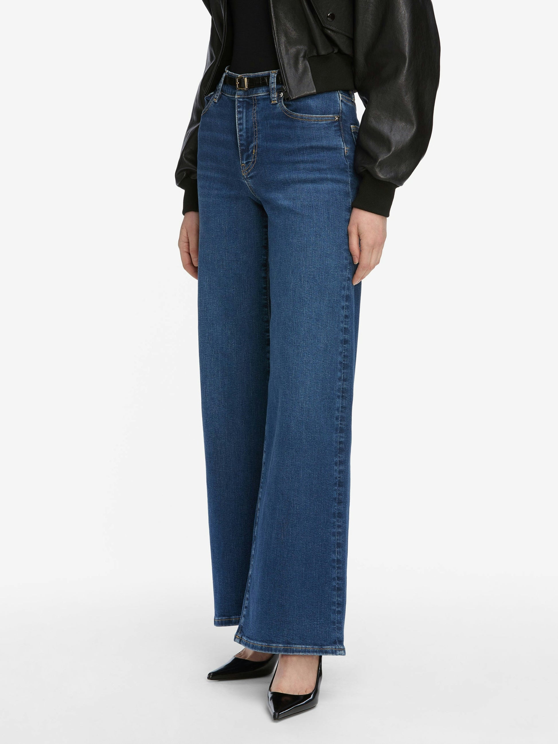 Model wearing Frame Le Slim Palazzo Jeans - Femma by Frame, styled with a black leather jacket and black pointed-toe heels, standing against a plain white background.