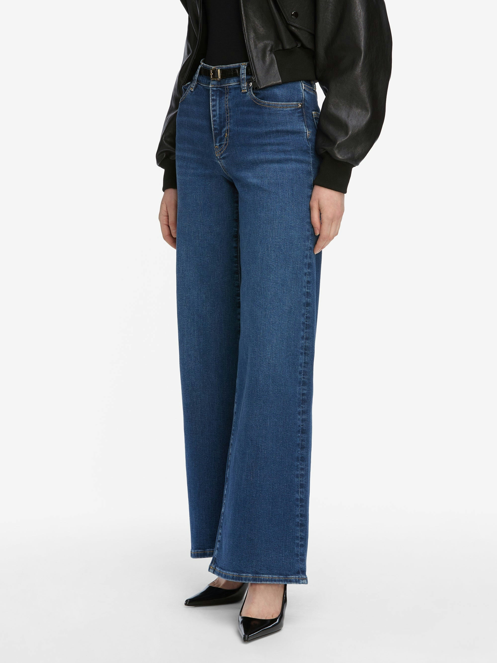 Model wearing Frame Le Slim Palazzo Jeans - Femma by Frame, styled with a black leather jacket and black pointed-toe heels, standing against a plain white background.