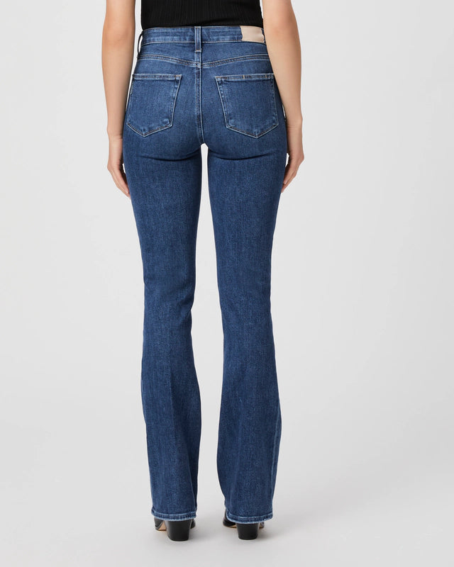 Person wearing blue denim jeans, viewed from the back. The Paige Laurel Canyon Bootleg - A Capella high-rise bootcut jeans have two back pockets and flare slightly at the bottom. The person is also wearing a black top.