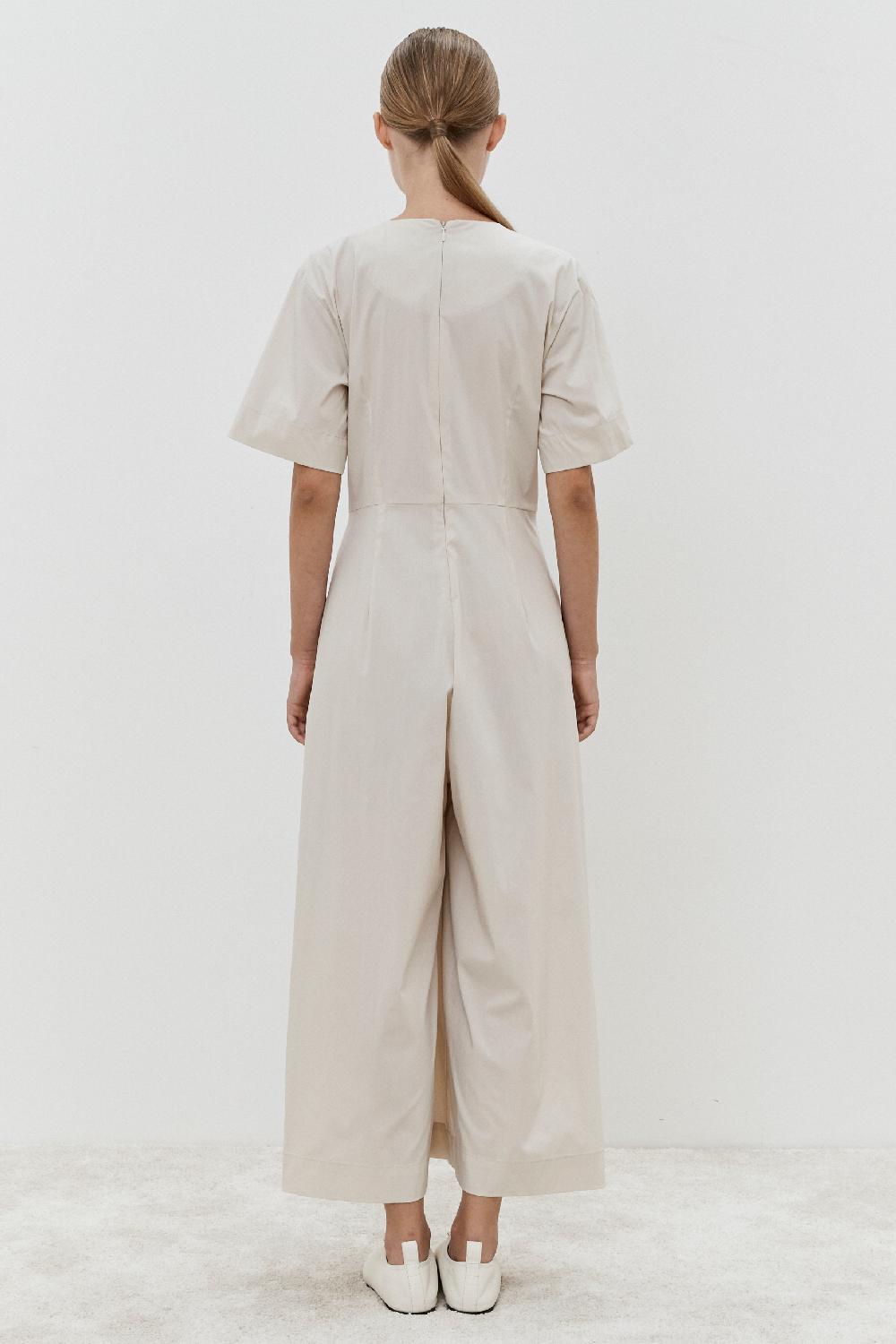 A person stands with their back to the camera in a MeiMeij Jumpsuit - Oyster, styled in Italian sizing, paired with white shoes against a light background.