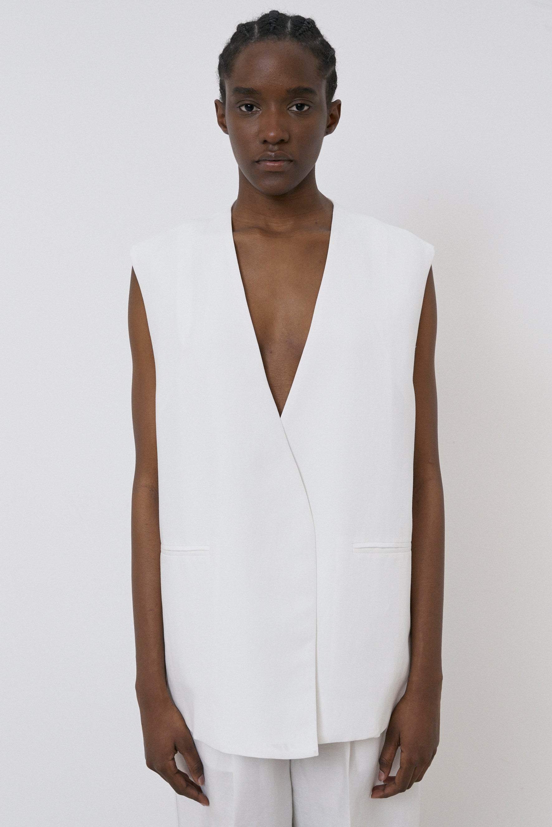 A person stands against a plain background, wearing the MeiMeij Oversized Vest in off white paired with modern fit white pants, looking directly at the camera.