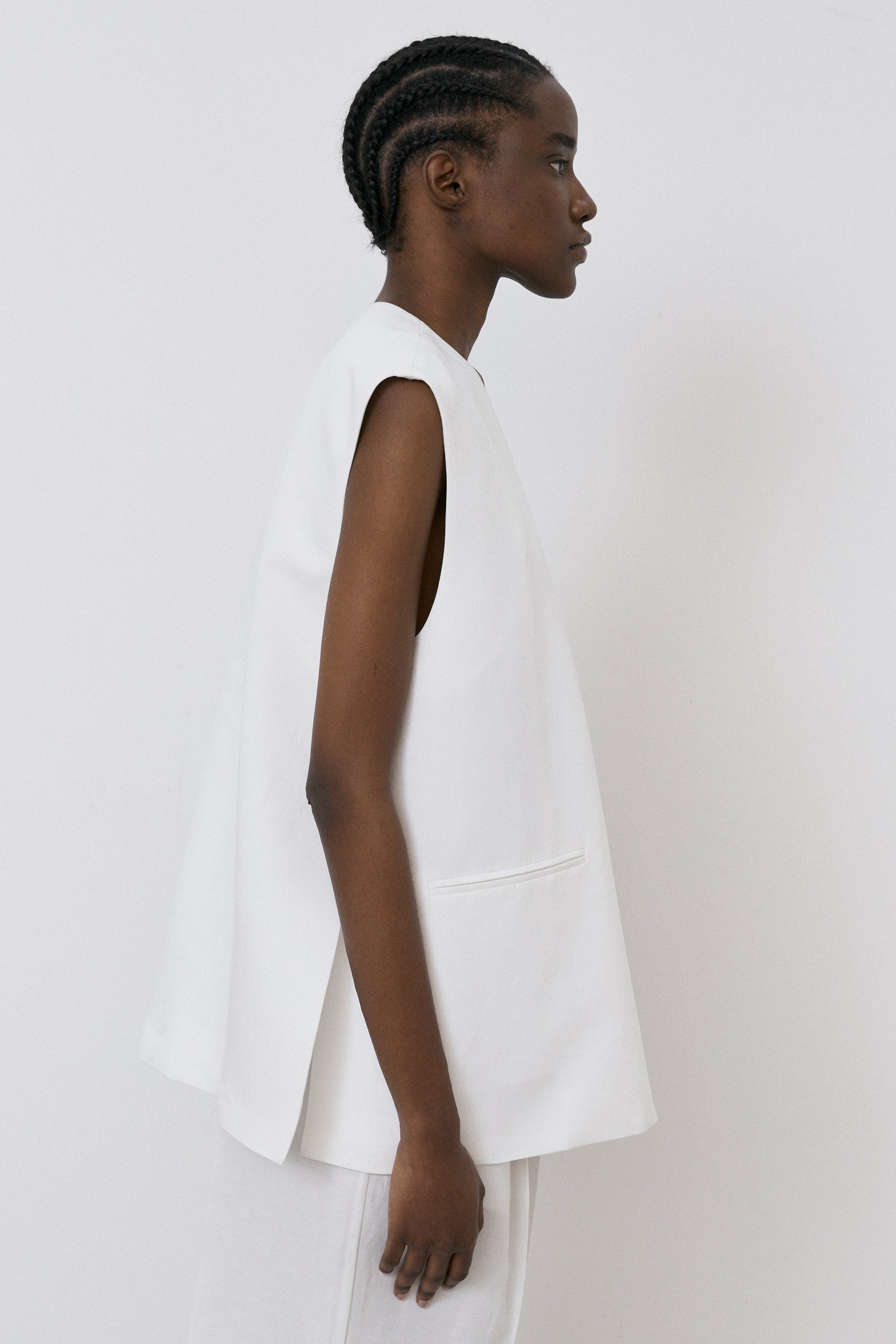 A person in profile models MeiMeij's Oversized Vest - Off White paired with white pants against a plain background, embodying the modern fit typical of Italian sizing.