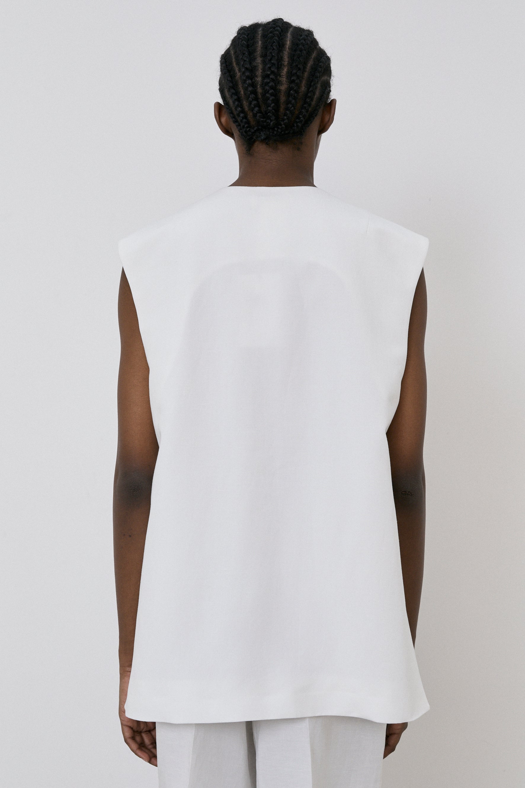 A person with braided hair is seen from behind, modeling an Oversized Vest in Off White by MeiMeij, paired with matching pants against a plain background.
