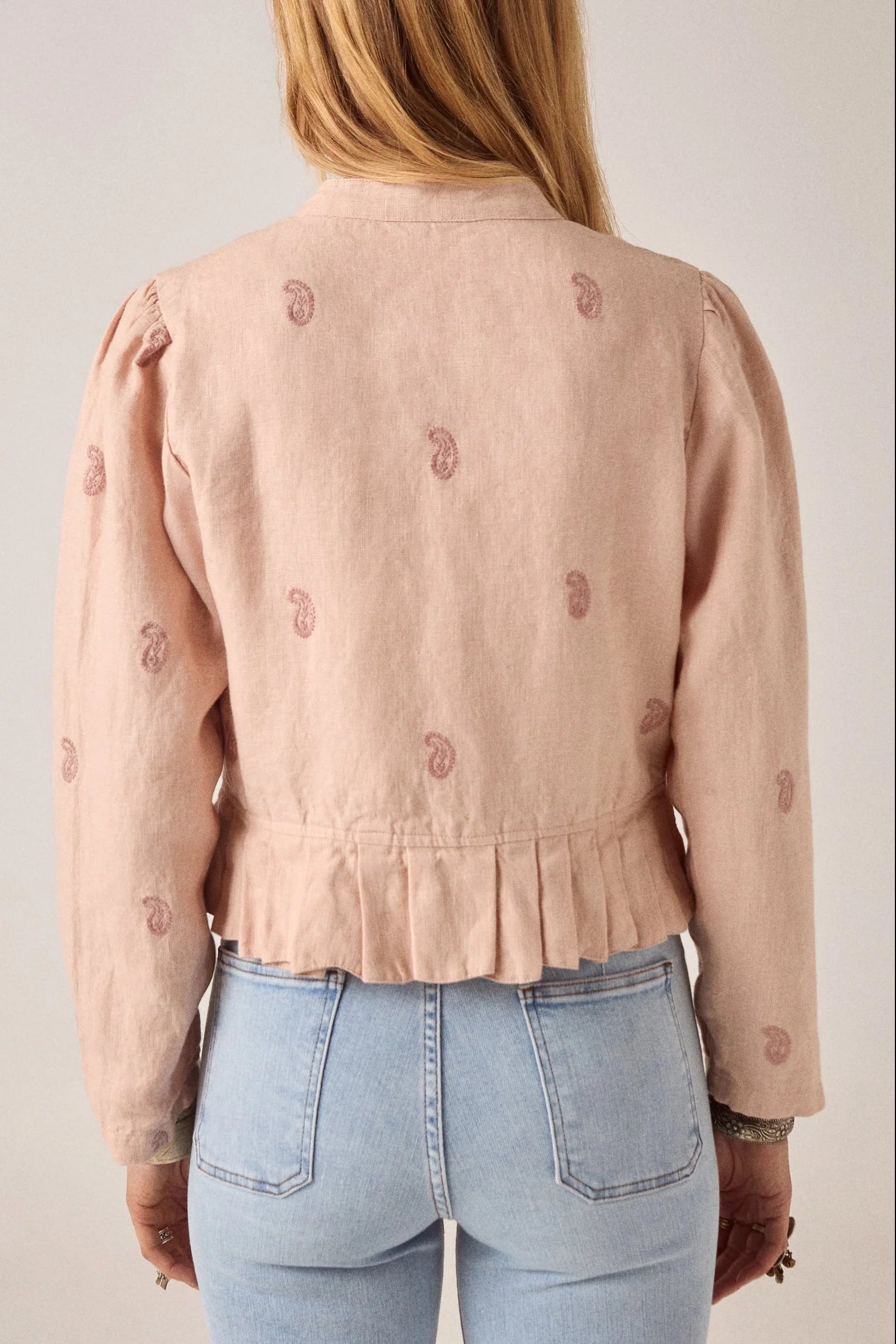 woman wears maison hotel edgar jacket in blush rose pink with light coloured jeans on a white background