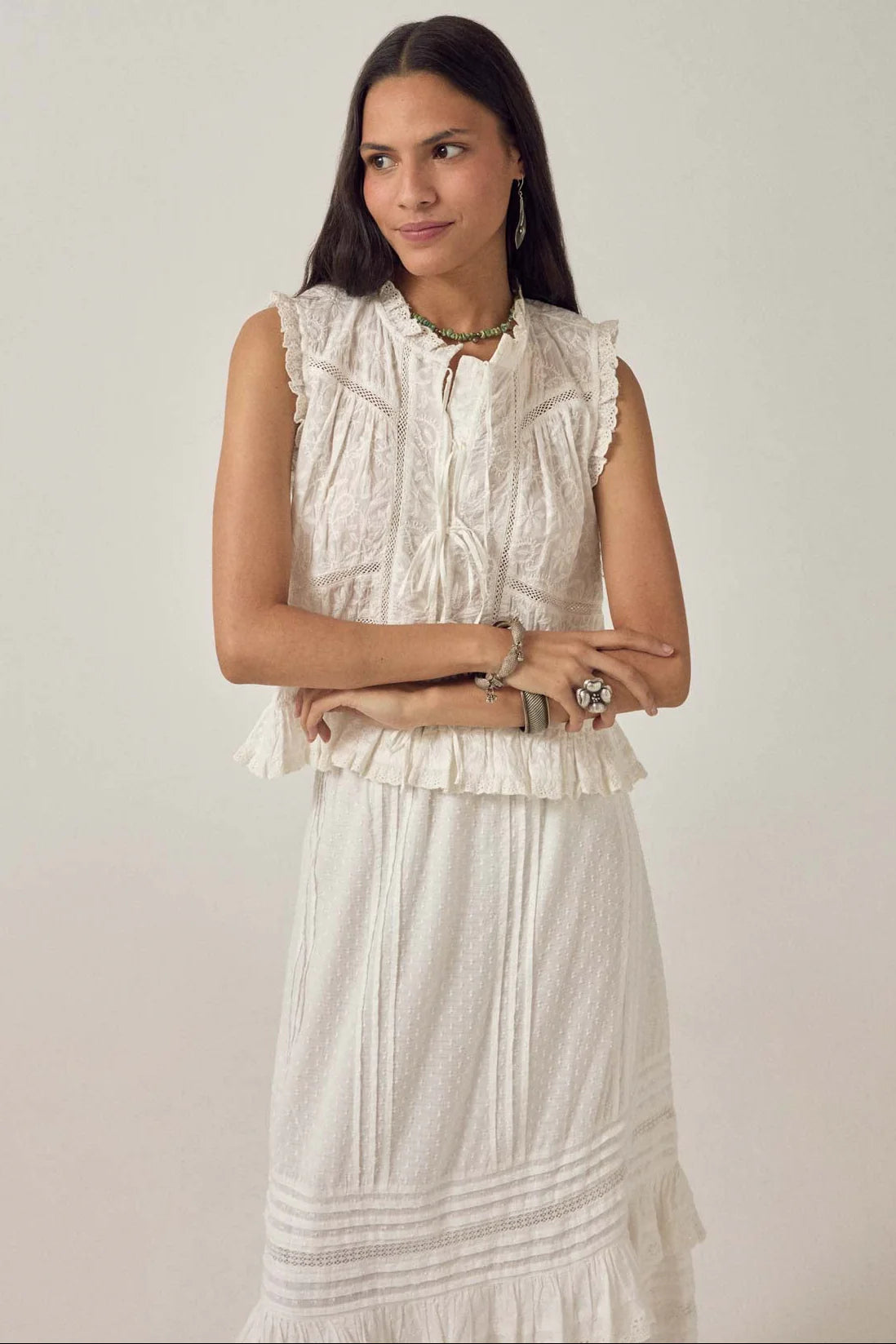 A woman stands against a plain background wearing the Maison Hotel Camila Top in Bright White, paired with a matching white skirt and jewelry.