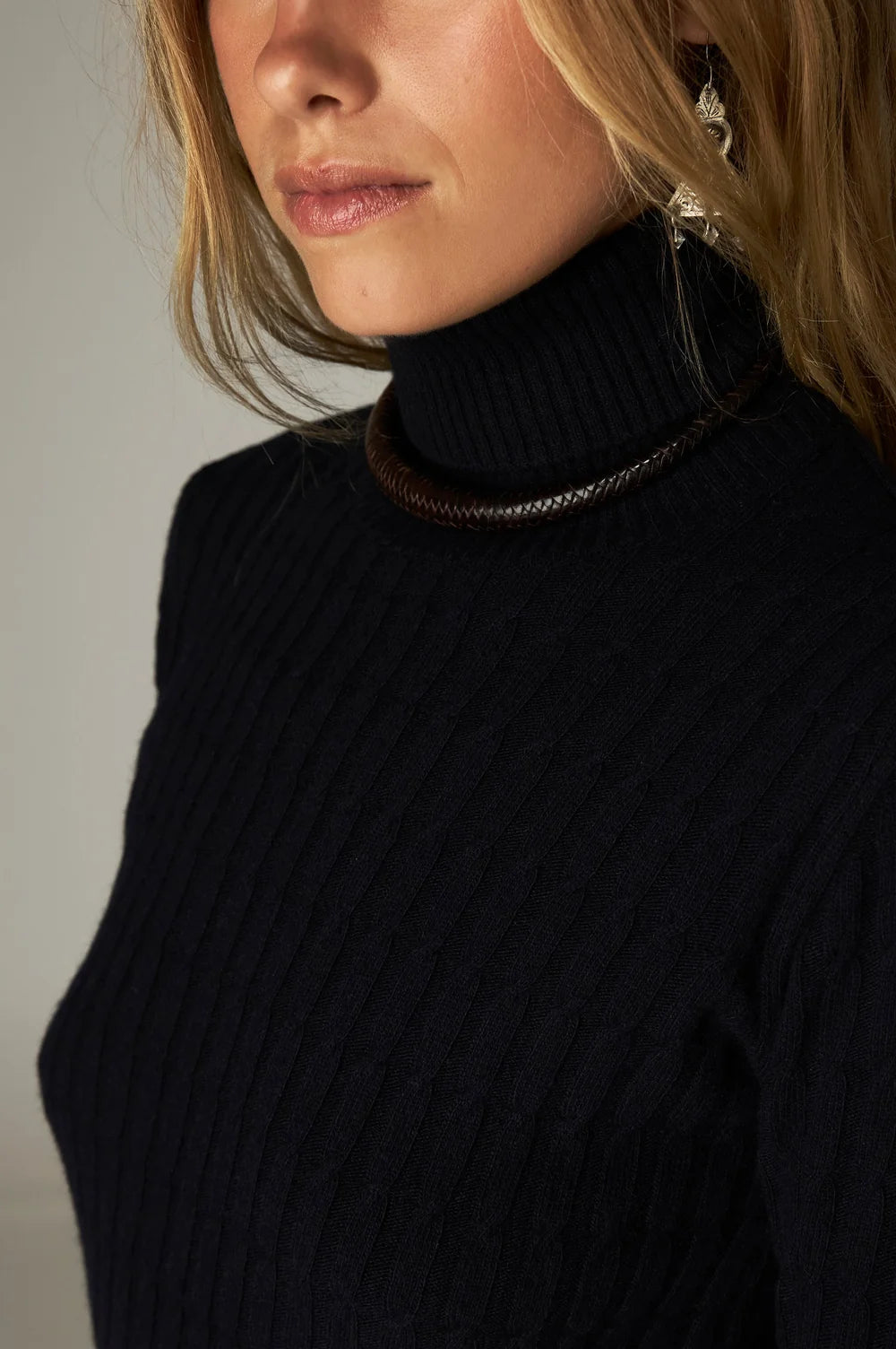 Close-up of a person wearing the Nancy Sweater - Black Frequency, featuring a black ribbed mock neckline and a dark woven choker necklace.