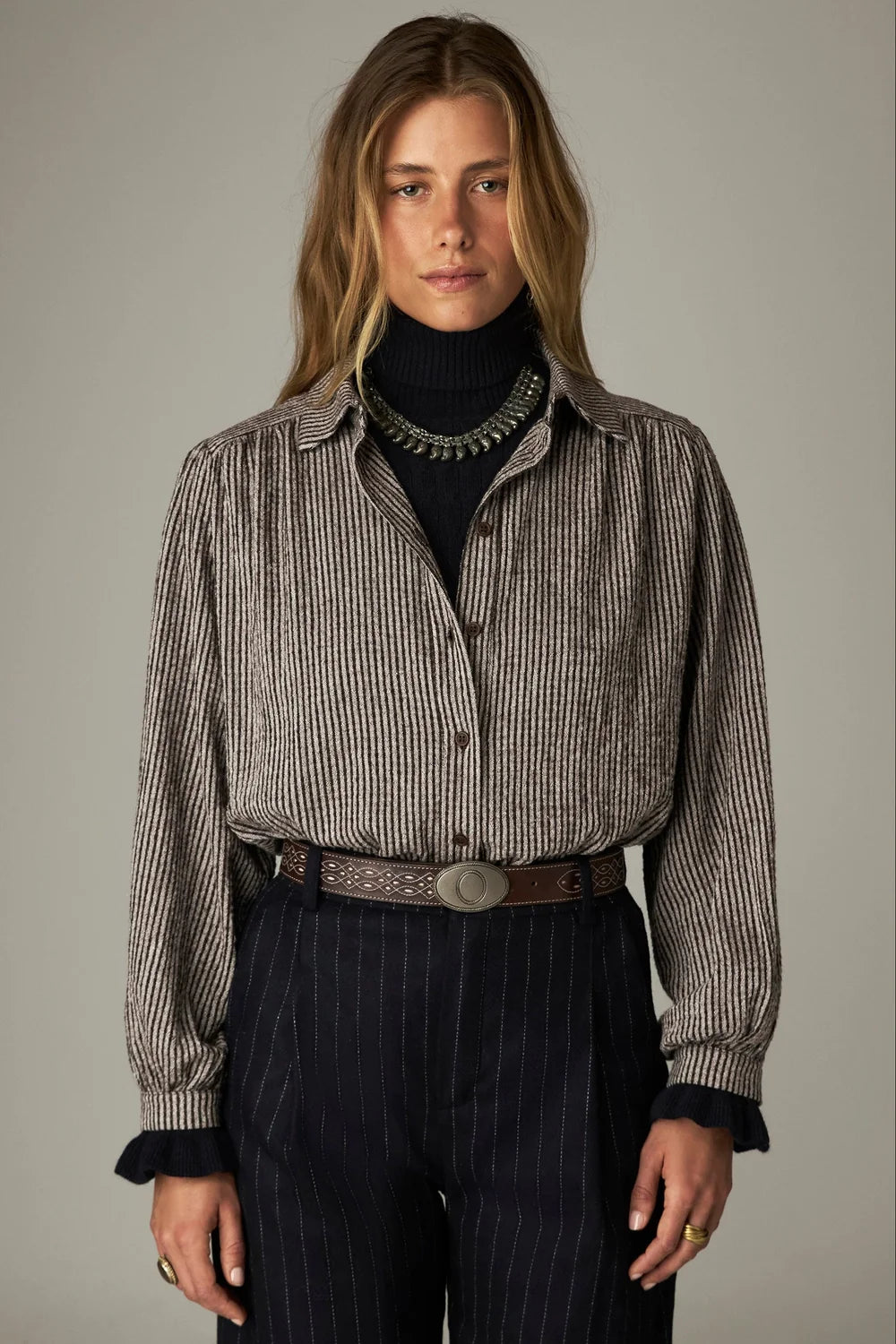 Claude Blouse - Coffee Stripes with a gathered yoke worn over a dark turtleneck and dark pinstriped trousers with a decorative leather belt.