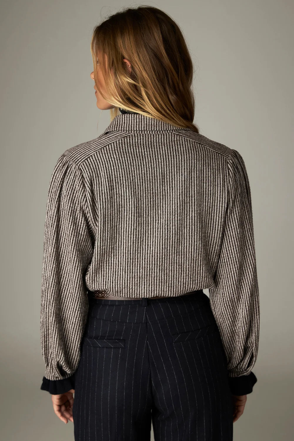 Back view of a person wearing a Claude Blouse - Coffee Stripes with puff shoulders and dark, pinstriped trousers.