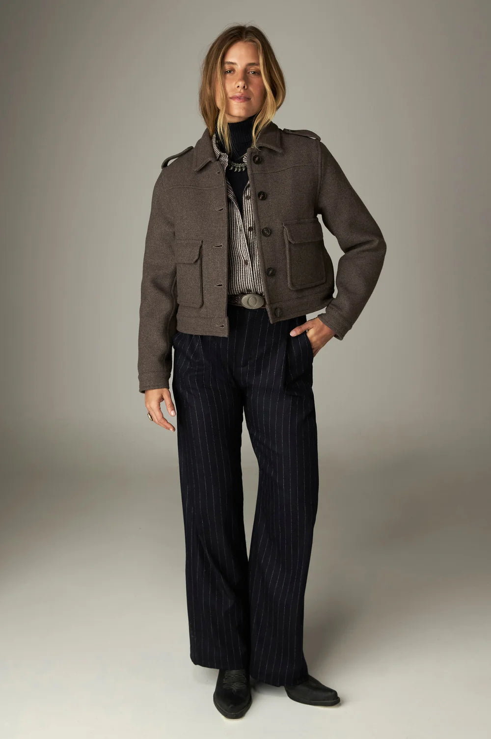 A person wearing a brown cropped jacket over a Claude Blouse - Coffee Stripes and high-waisted navy pinstripe trousers.
