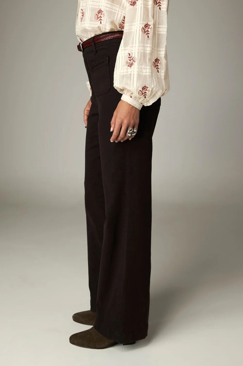 A person wearing the coffee-colored Giulietta Pant - Coffee high-rise wide-leg trousers, a cream patterned blouse, and brown suede boots.