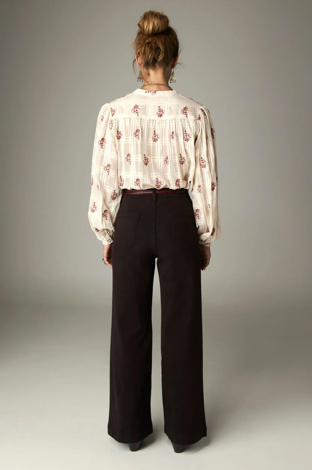 A person seen from behind wearing a white patterned blouse tucked into high-rise wide-leg Maison Hotel Giulietta Pant in coffee.