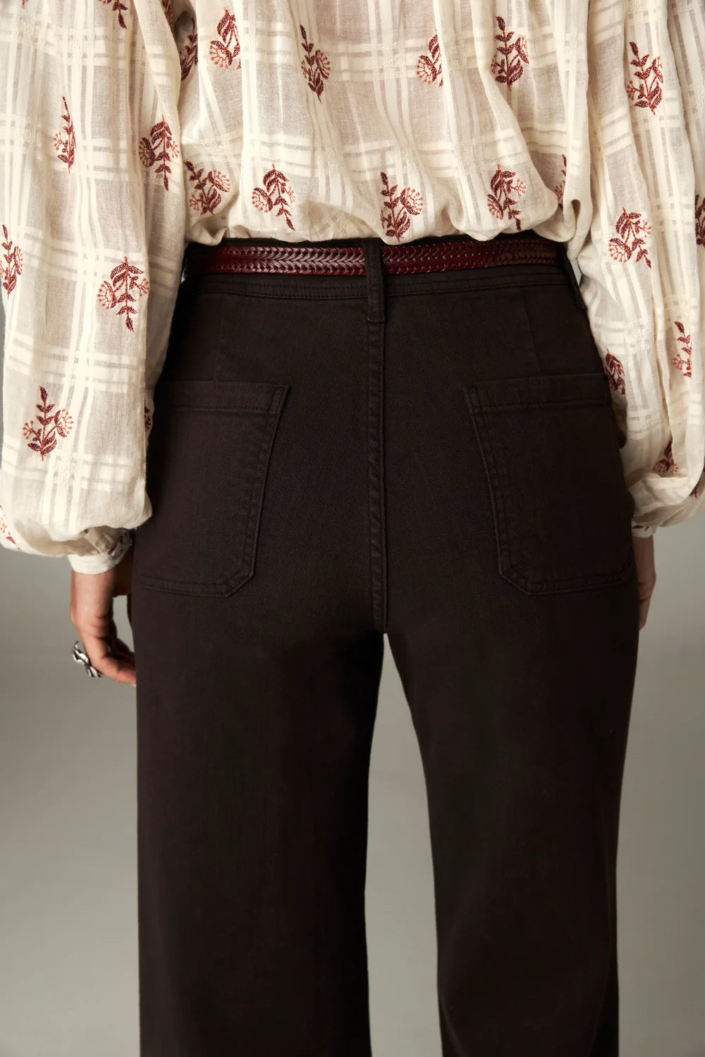 Maison Hotel Giulietta Pant in coffee, a high-rise, wide-leg style with back patch pockets and a braided belt, worn with a cream-colored patterned blouse.