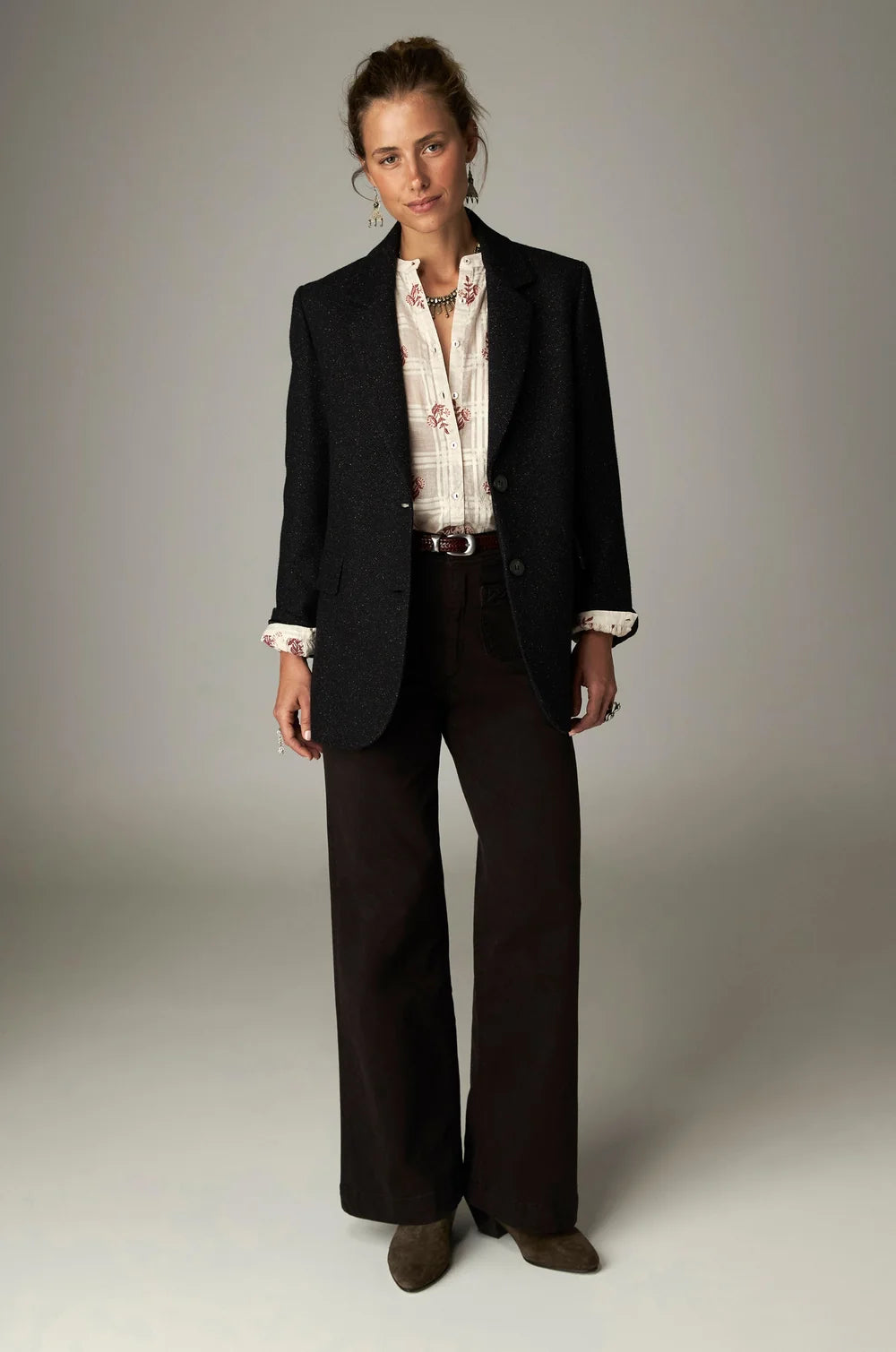 A person wearing a black blazer over a patterned white button-down shirt, brown high-rise wide-leg Giulietta Pant - Coffee, and brown ankle boots.