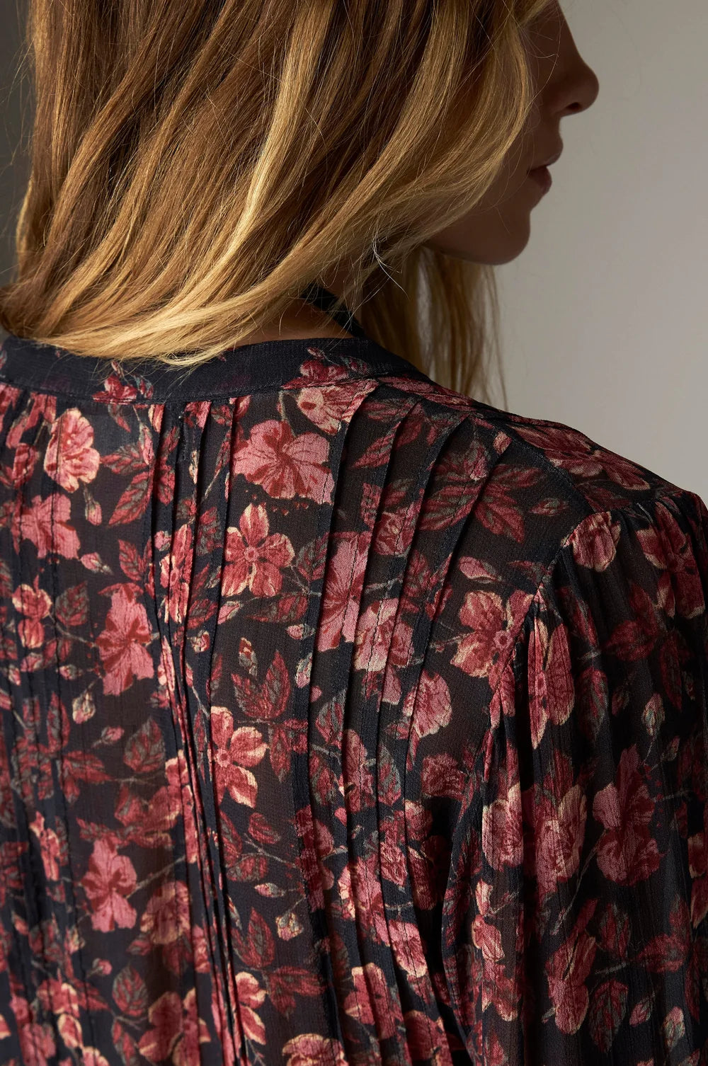 A woman wearing the Lerele Blouse - Punk Pink, a bohemian, pleated blouse featuring a dark floral print in shades of pink and black with a relaxed silhouette.