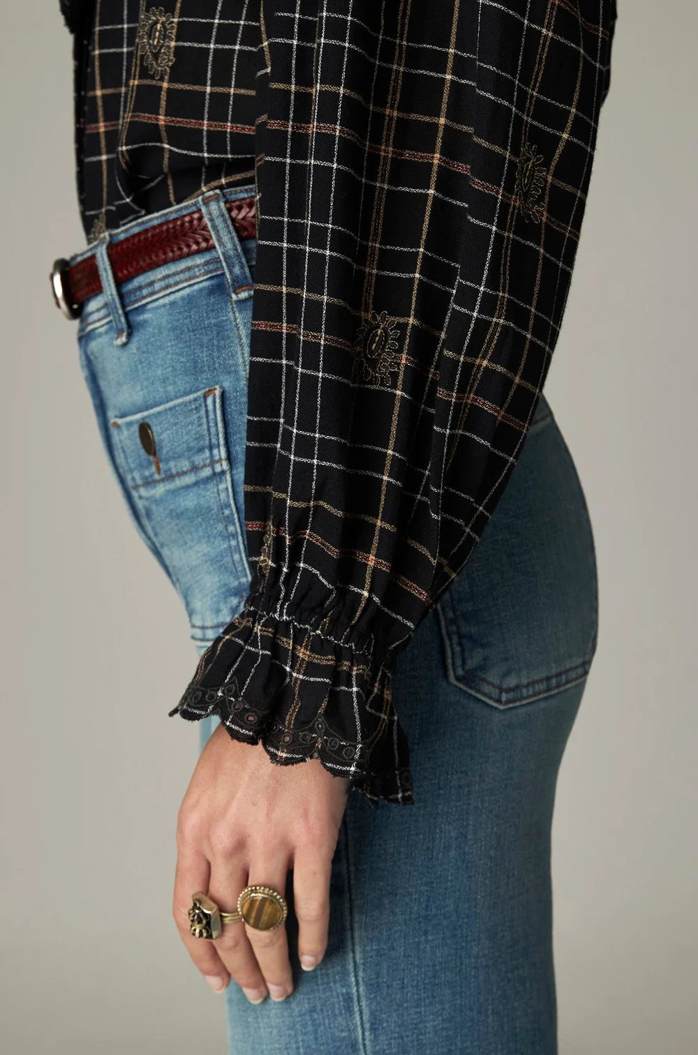 Maison Hotel Coco Blouse - Noir Plaid, a black long-sleeved plaid top with gold embroidery, tucked into blue jeans with a brown leather belt.