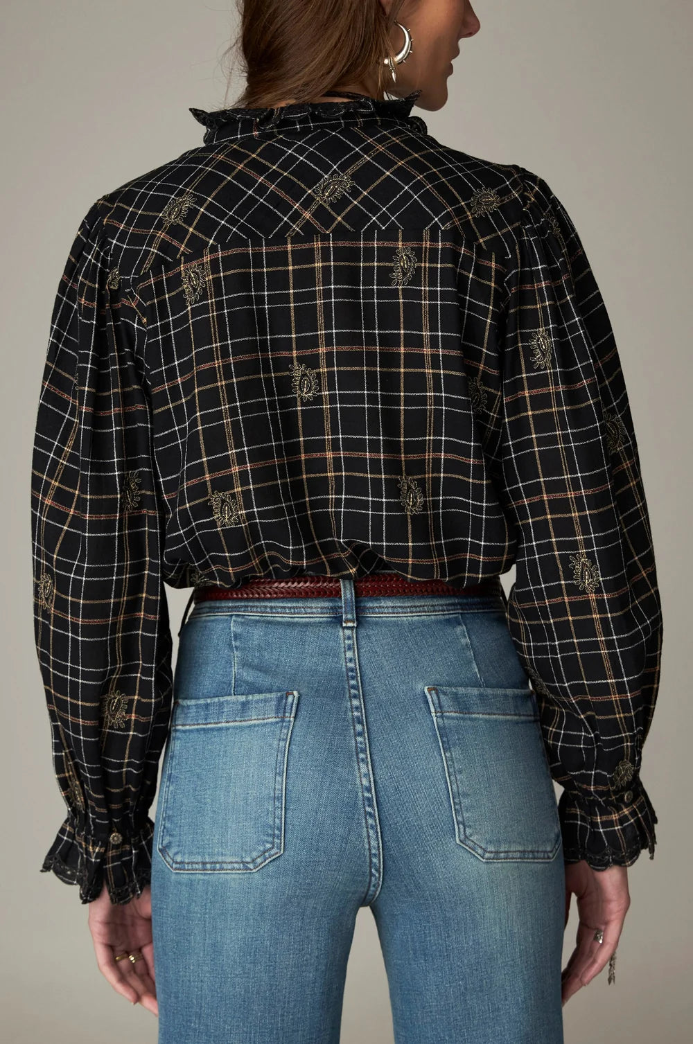 Maison Hotel Coco Blouse - Noir Plaid, a black long-sleeved shirt with small floral embroidery tucked into blue jeans with a thin brown belt.