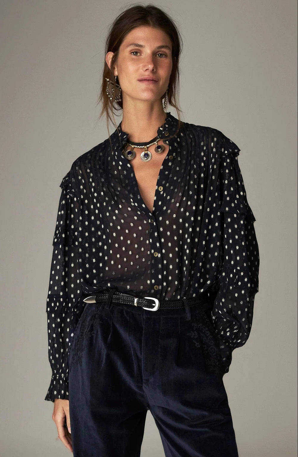 Maison Hotel Simona Blouse - Sienna navy: a semi-sheer, long-sleeved navy blue metallic jacquard blouse with a white polka dot pattern, tucked into dark trousers with a black leather belt.