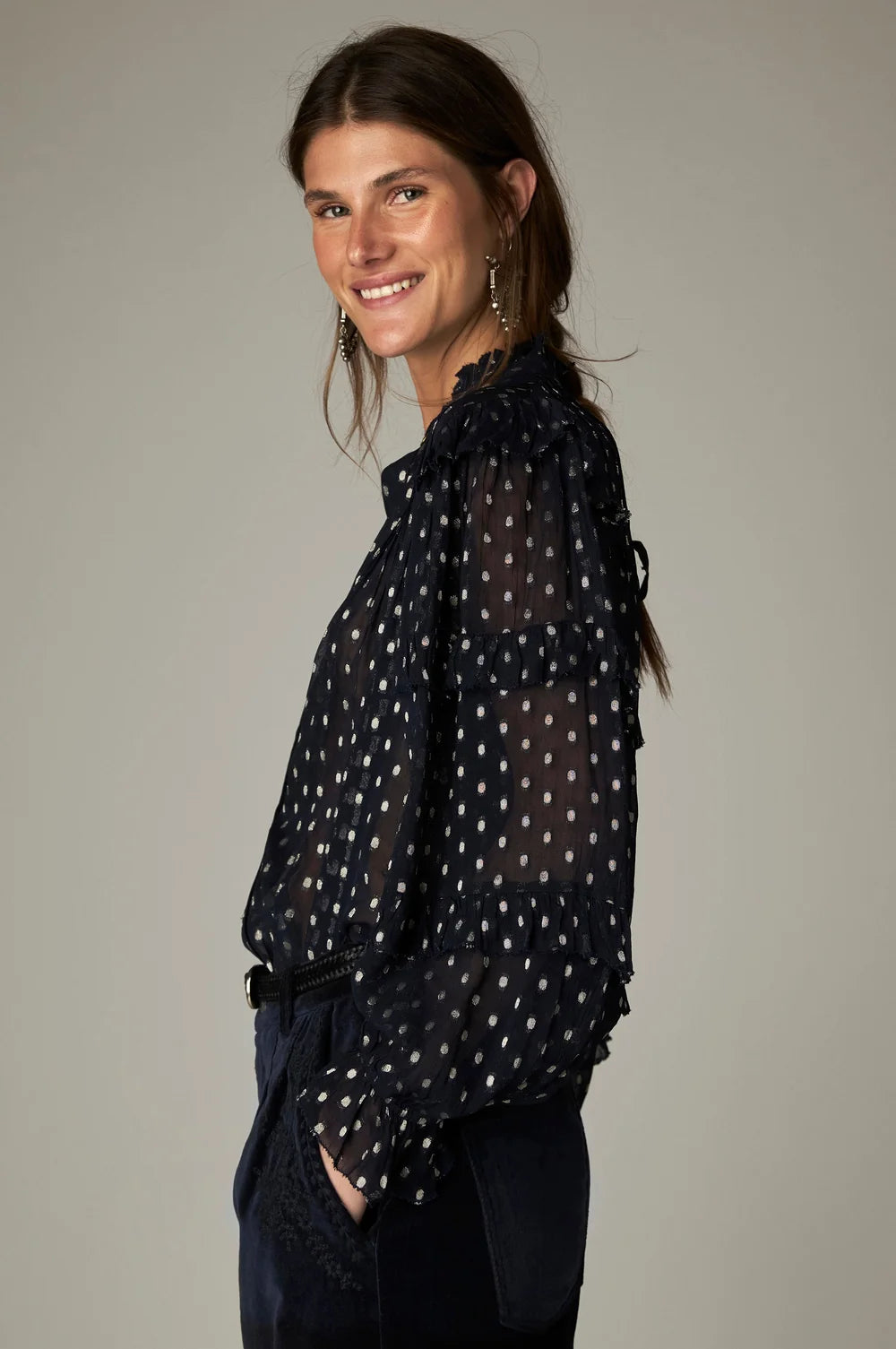 A woman wearing the Maison Hotel Simona Blouse - Sienna navy, a sheer, long-sleeved navy blue blouse with white polka dots and ruffle detailing that captures a bohemian aesthetic.