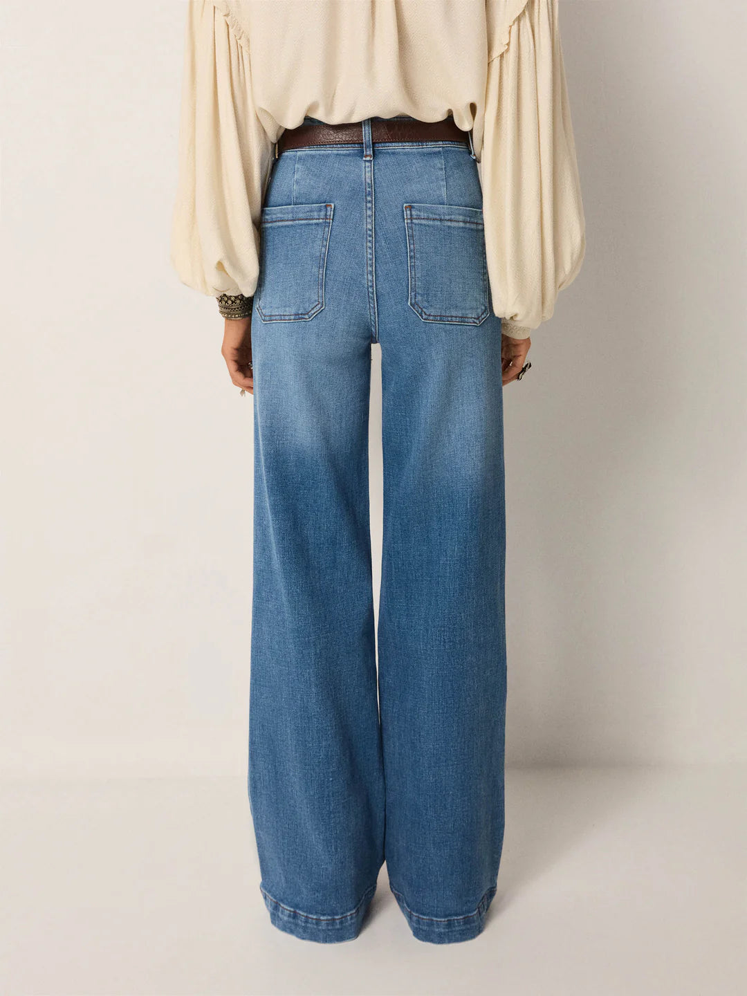 A person is shown from the back wearing Maison Hotel's Giuletta Trousers in light blue, styled with a cream long-sleeve blouse against a plain background.