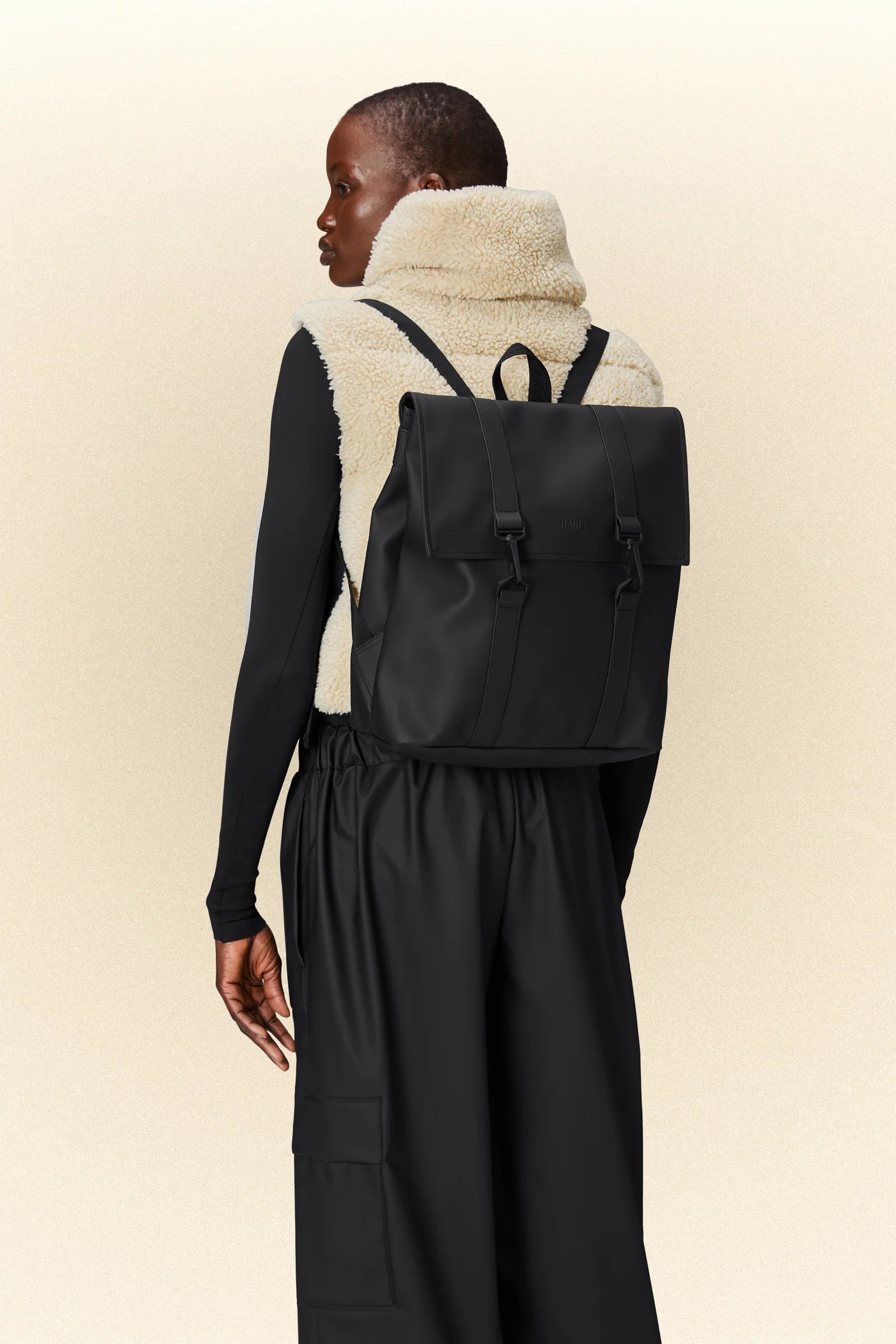 The back of a woman wearing a black Rains MSN Bag Mini classic school backpack.