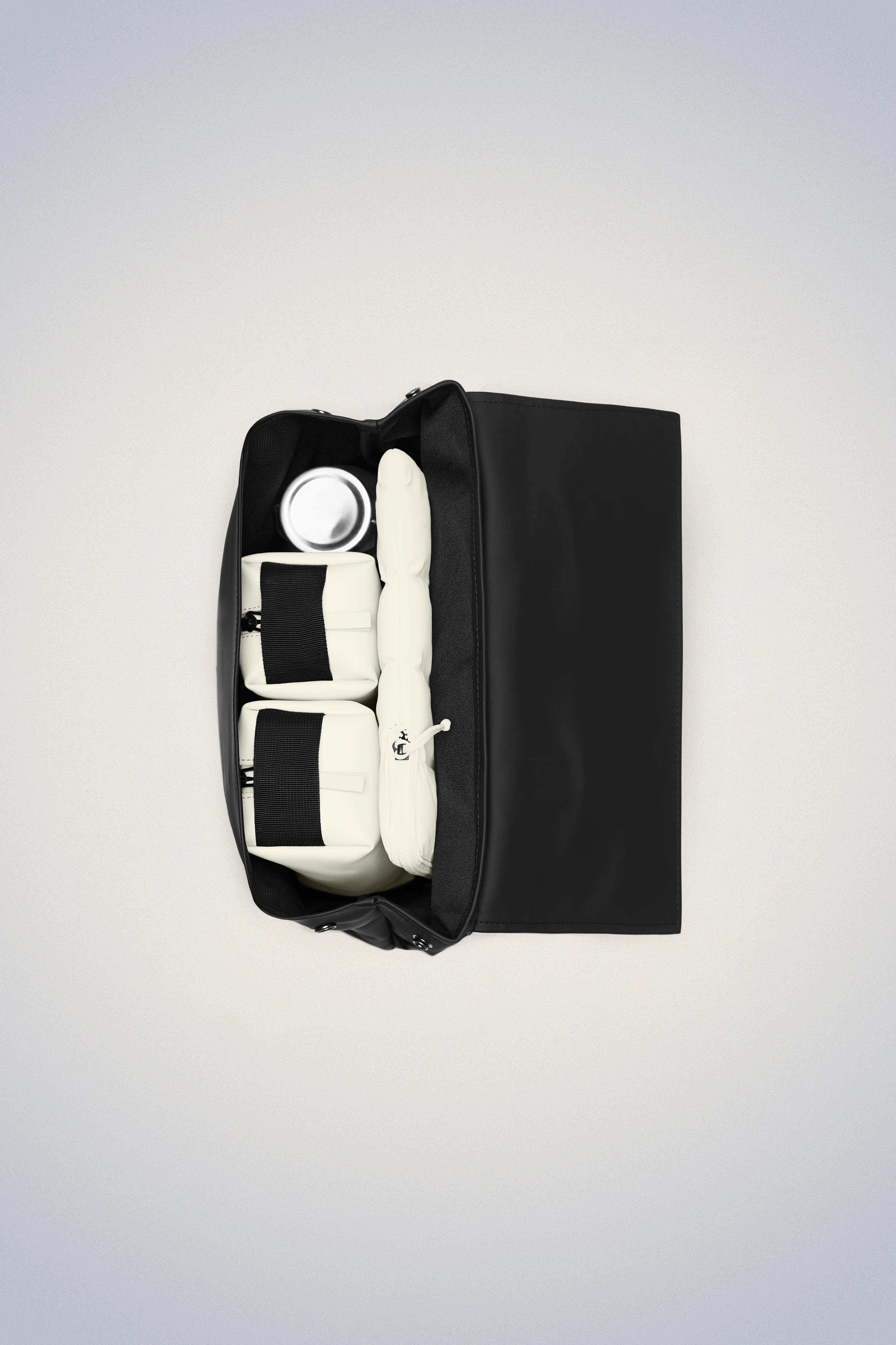A classic school backpack, the Rains MSN Bag Mini, in black and white with a few conte items inside.