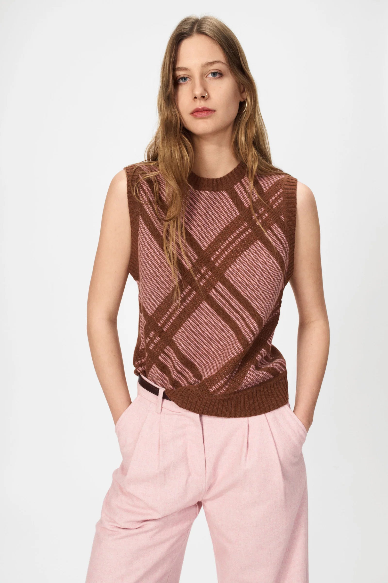 A woman stands with hands in pockets, wearing the Nué Notes Malik Vest in Chestnut Pink and light pink pants against a plain background.