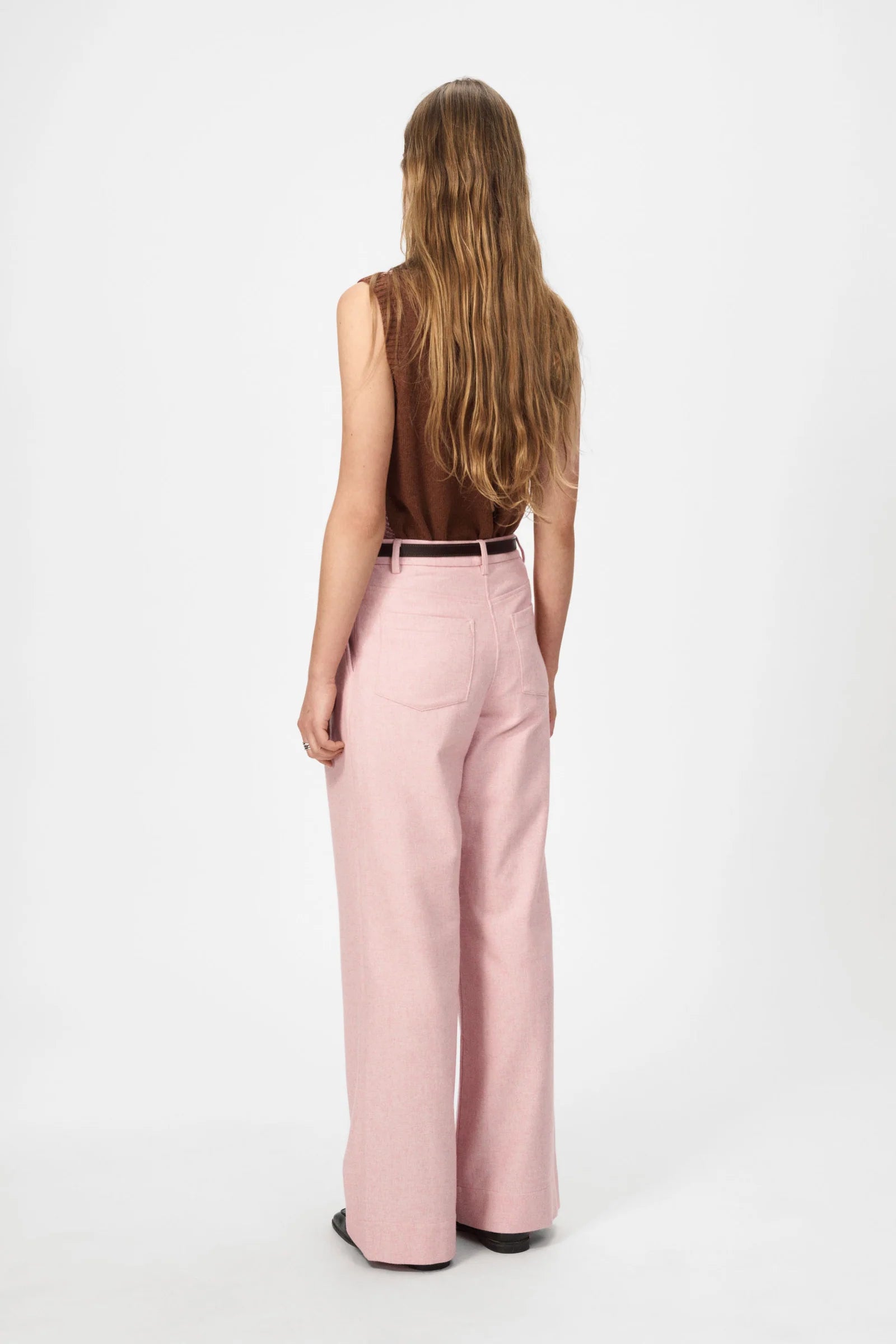 A person with long hair, wearing the Nué Notes Malik Vest in Chestnut Pink, stands facing away against a plain white background.