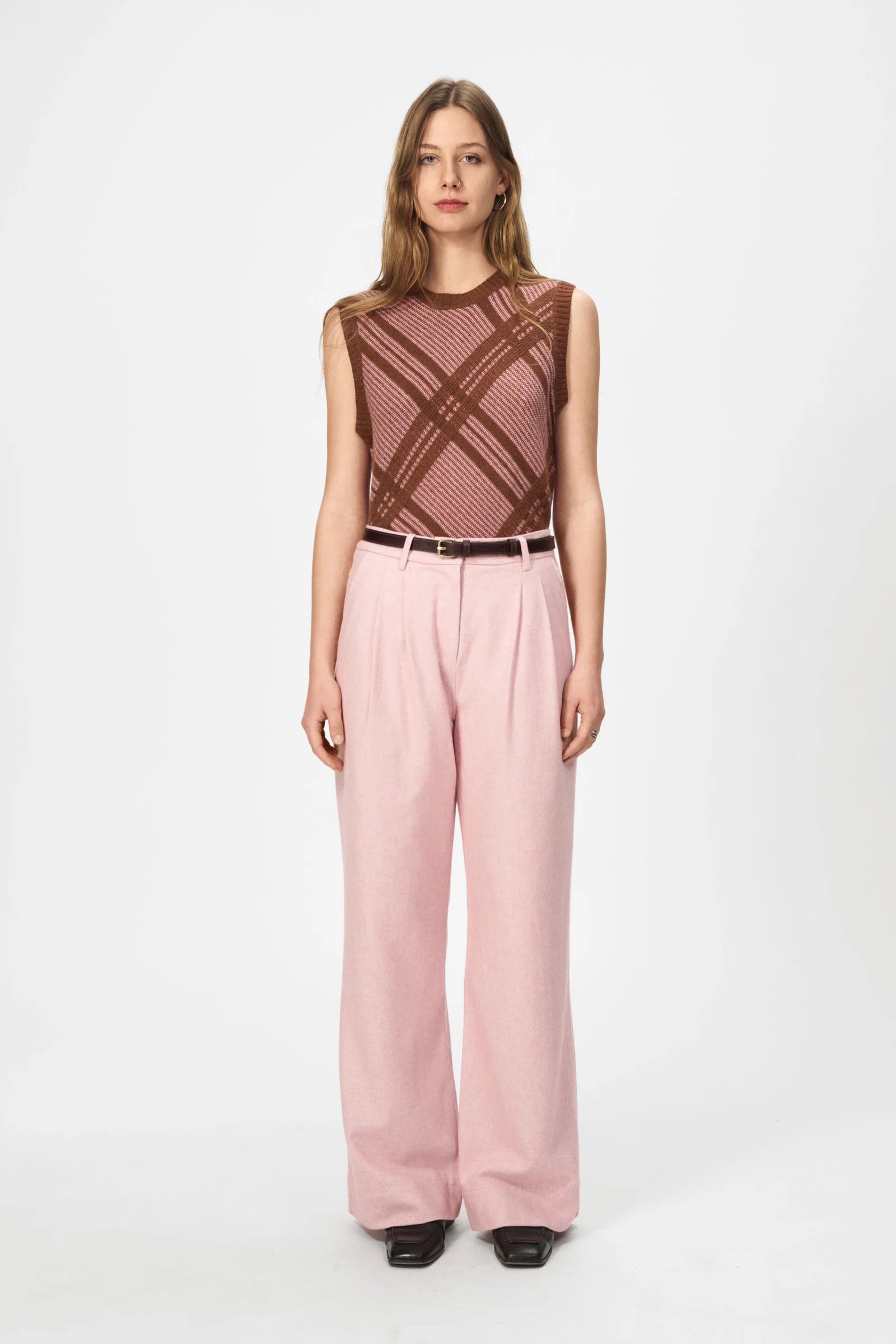 A woman faces forward wearing the Nué Notes Malik Vest in Chestnut Pink, styled with light pink wide-leg trousers and black shoes against a plain white background.