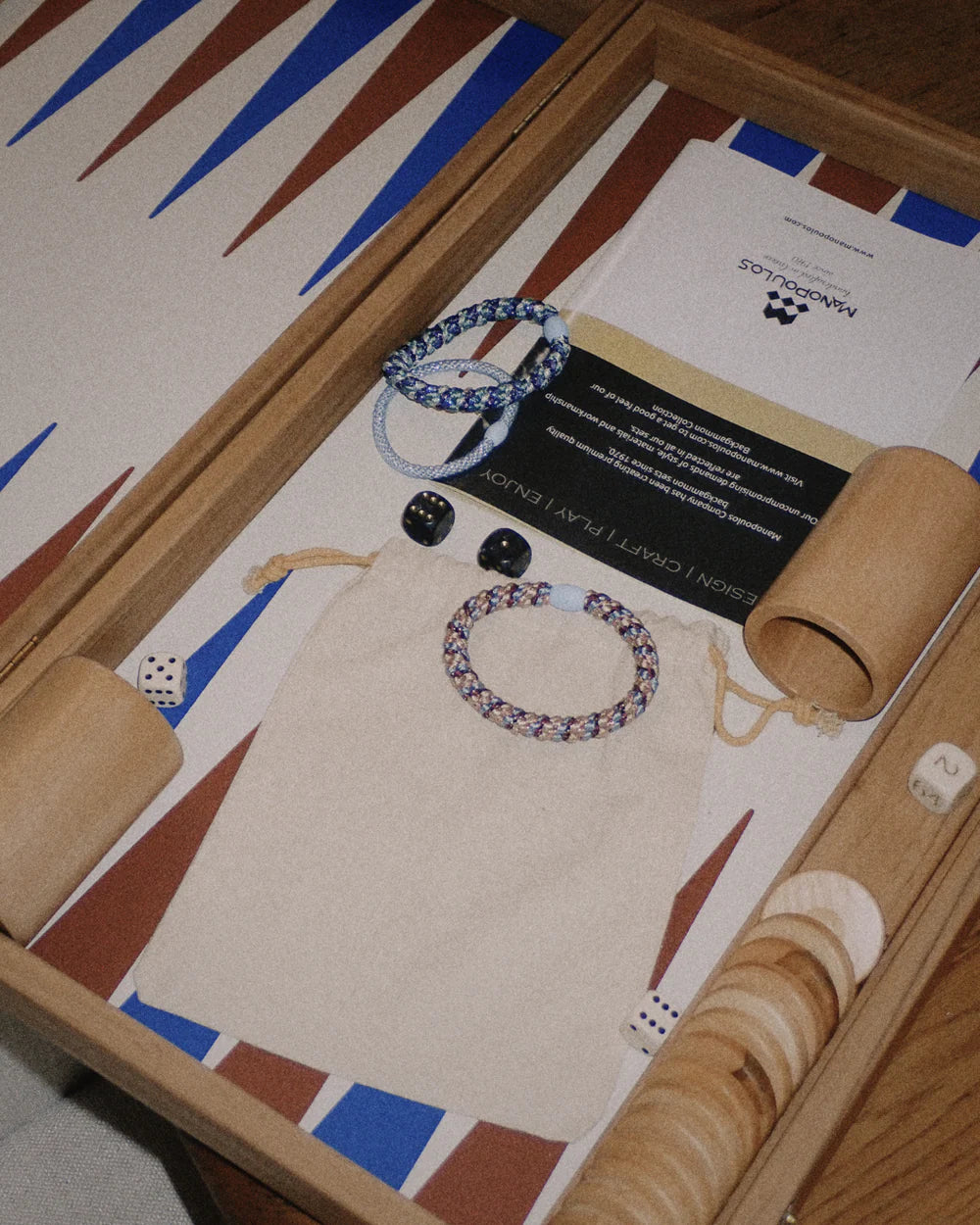 An open backgammon set with dice, wooden chips, rolling cups, a pouch, two KKNEKKI Hair Tie - Mix gentle grip hair ties, and informational cards on the board.